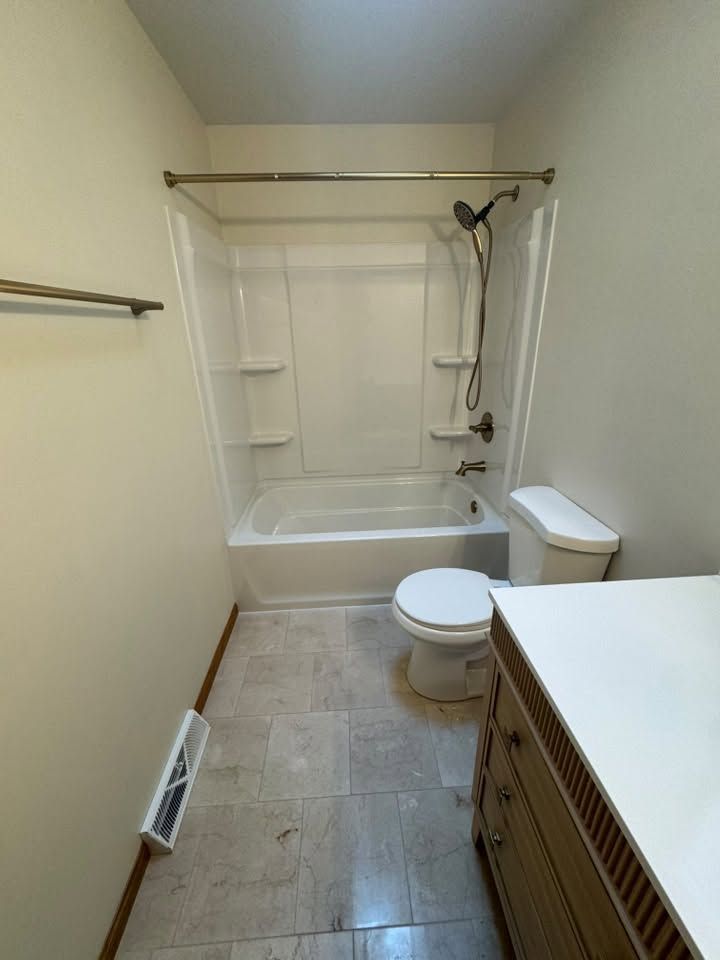 Small beige bathroom with a bathtub-shower, toilet, sink vanity, and wall heater.