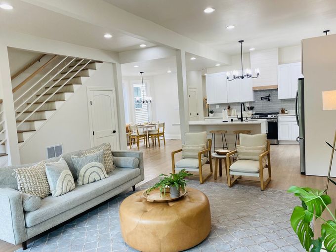 Bright open-concept living room with gray sofa, round ottoman, dining area, and kitchen.