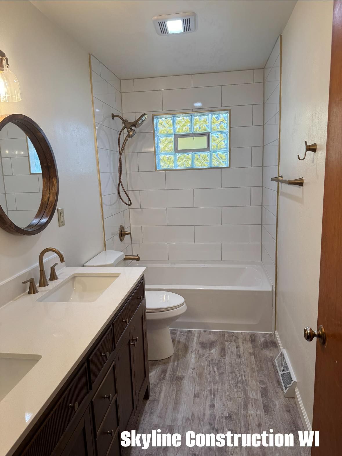 Small bathroom with white tile, vanity, toilet, tub, and a window above the shower.