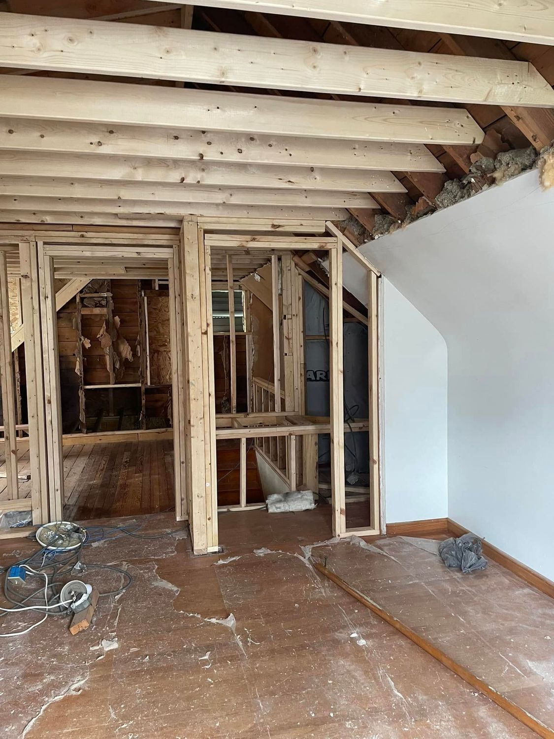Interior room under renovation with exposed wooden framing, beams, and unfinished floor.