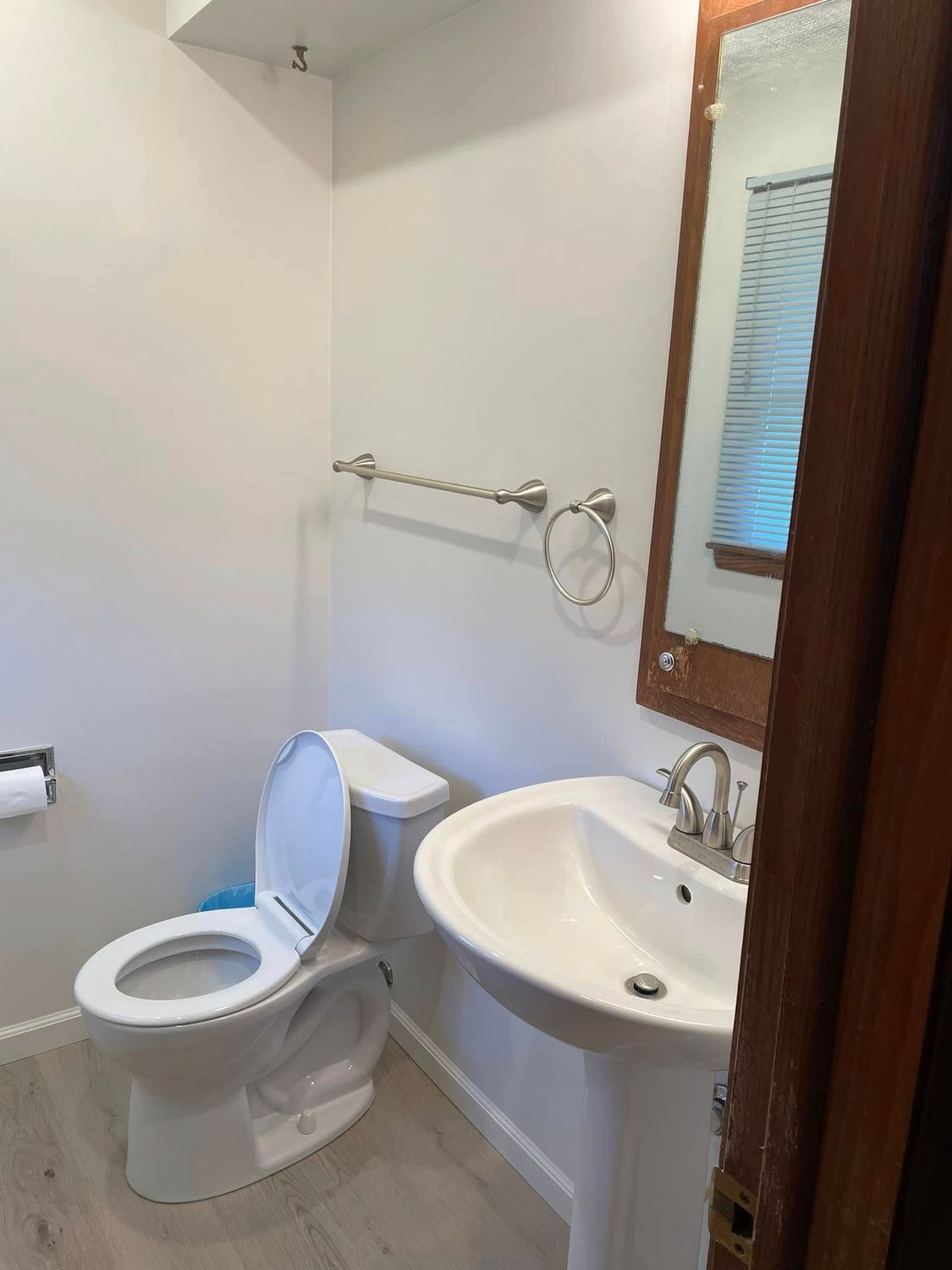Small bathroom with a toilet, pedestal sink, mirror, and towel rack.