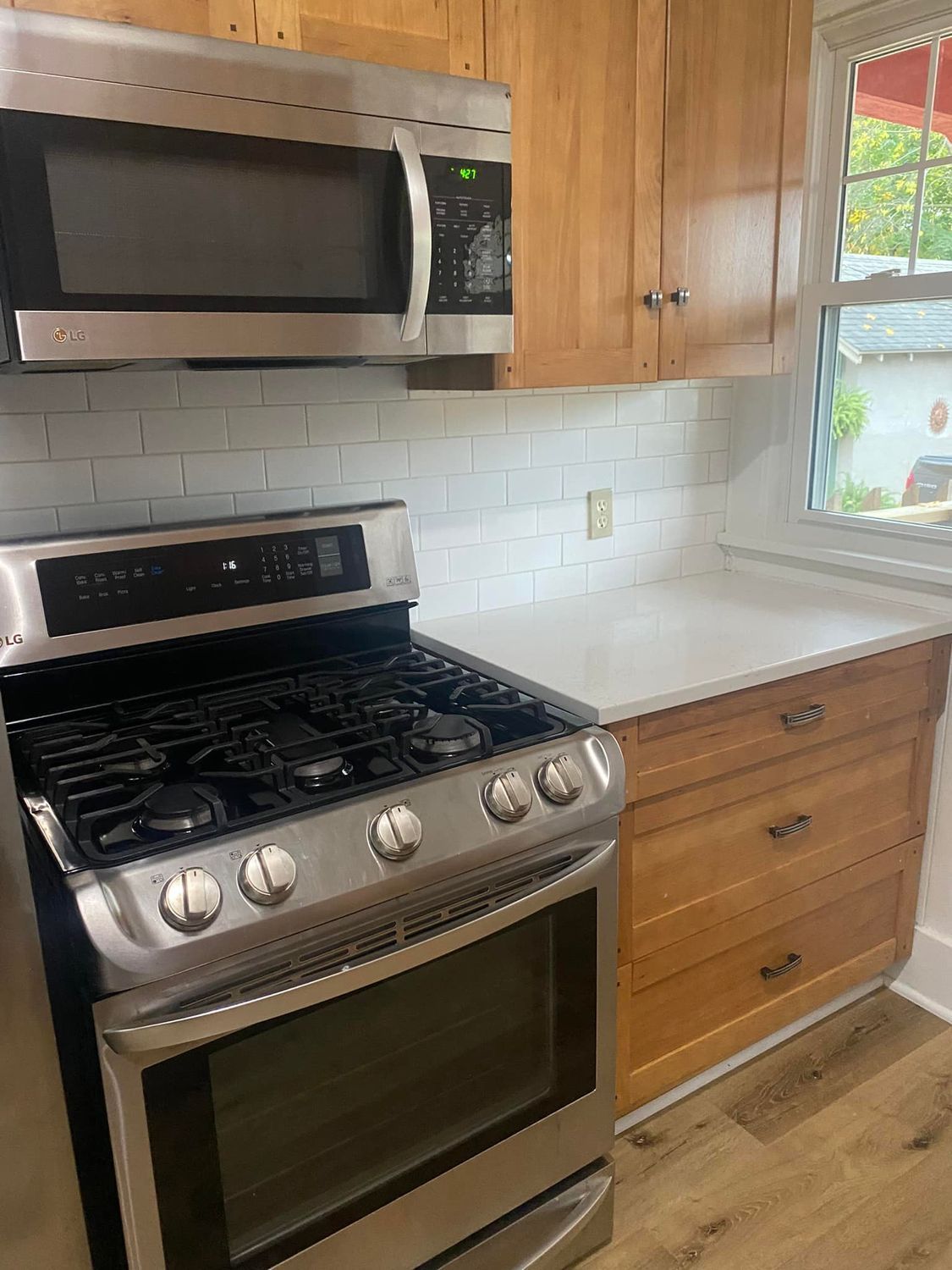 Modern kitchen with stainless steel stove and microwave, white tile backsplash, and wood cabinets