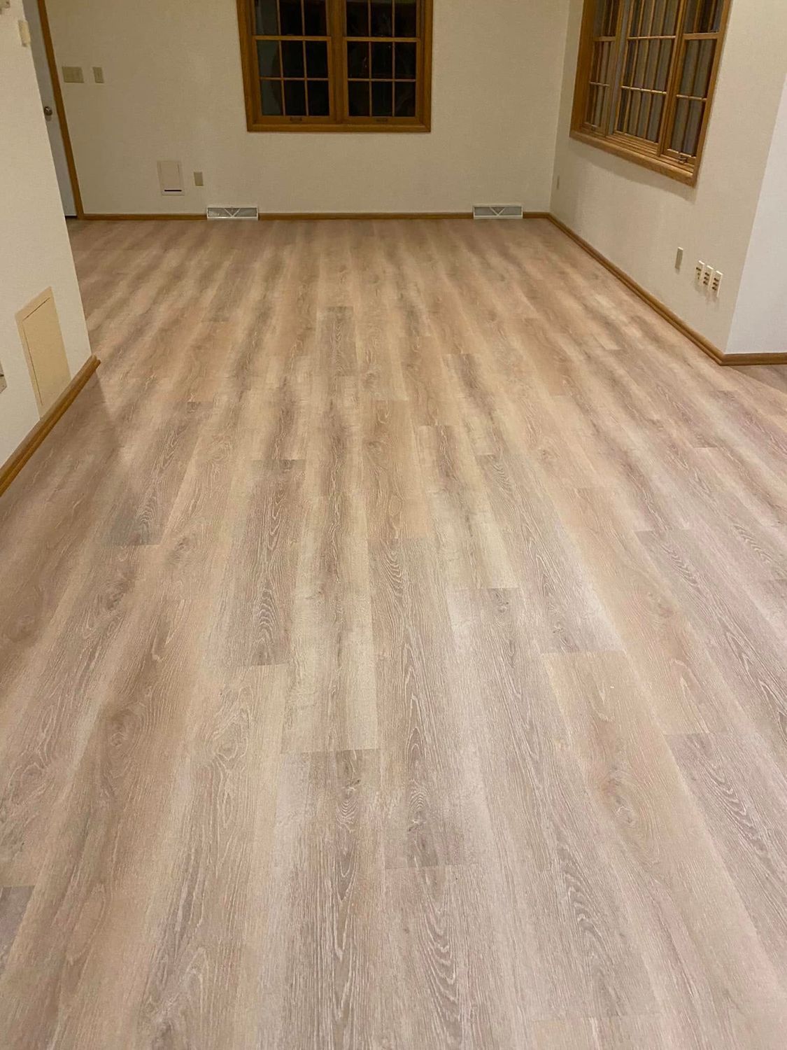 Empty room with light wood flooring, beige walls, and windows on the far wall.