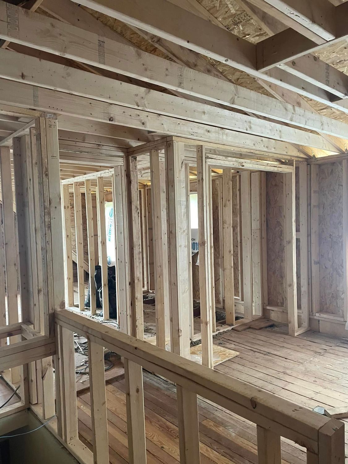 Unfinished wooden house interior with exposed studs, beams, and floor framing.