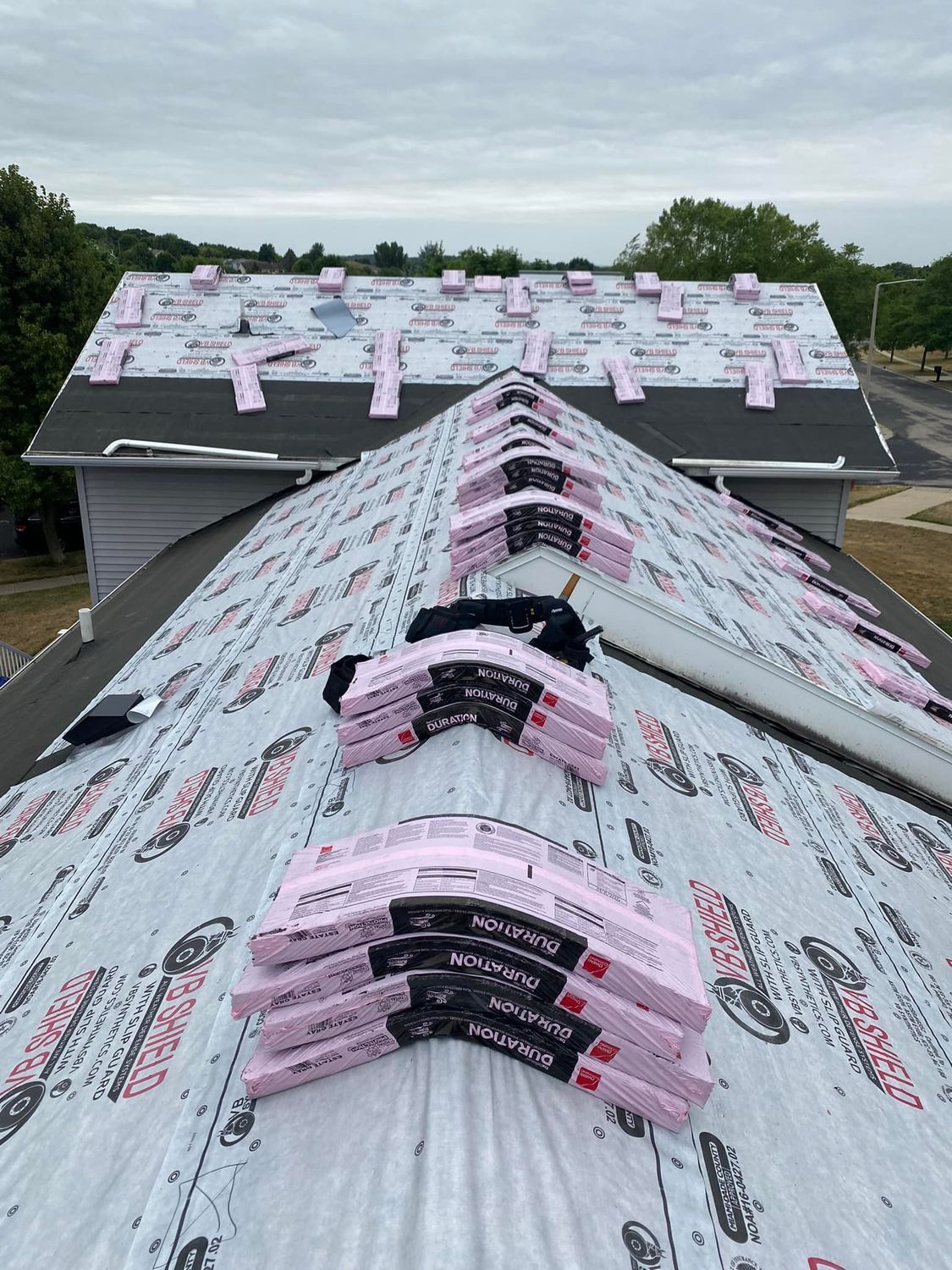 Roof under construction with pink and black roofing materials stacked along the ridge