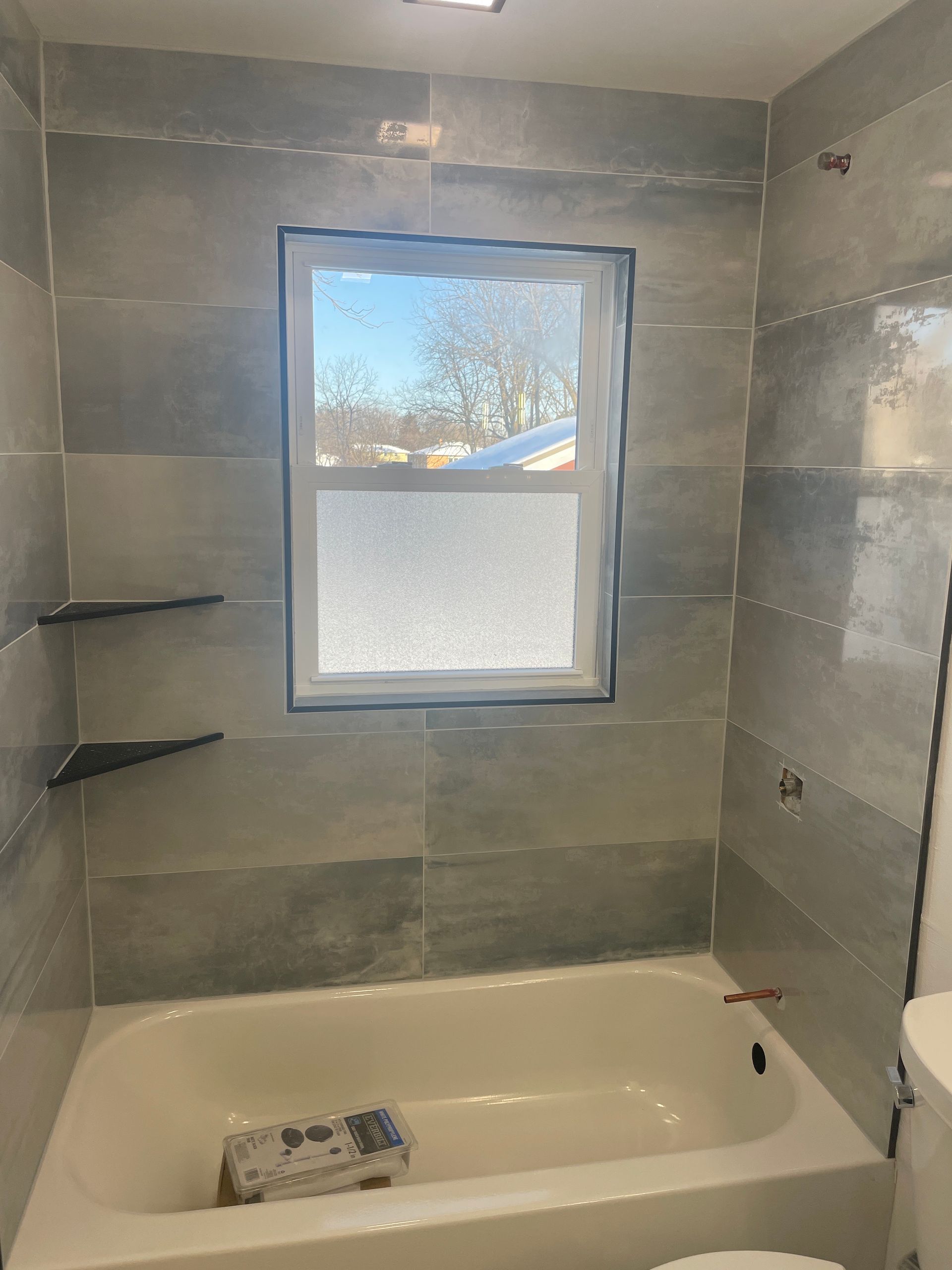 Bathroom shower tub with gray tile walls and a frosted window above the tub