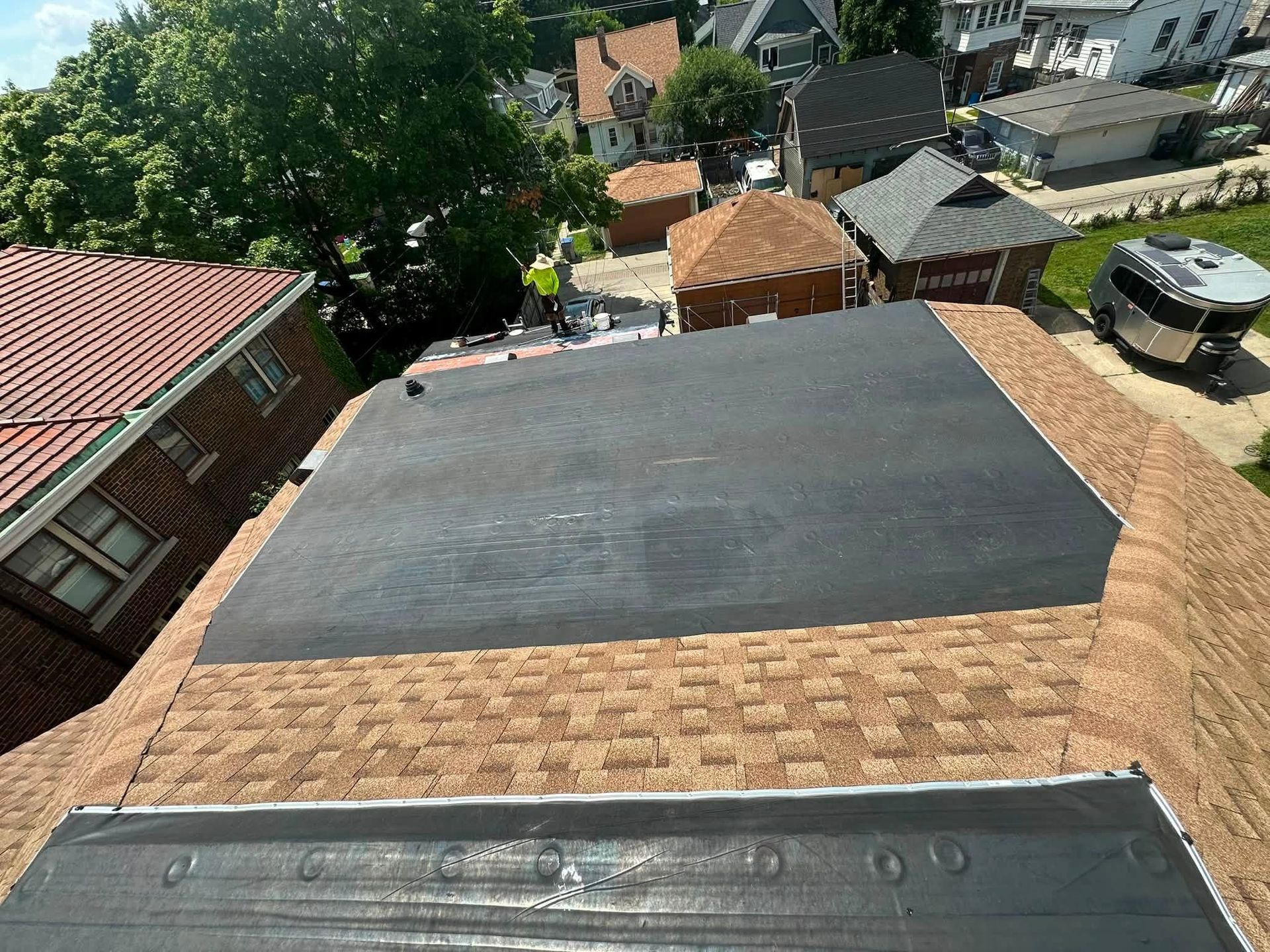 Rooftop view with a newly installed black flat roof and surrounding houses in a neighborhood