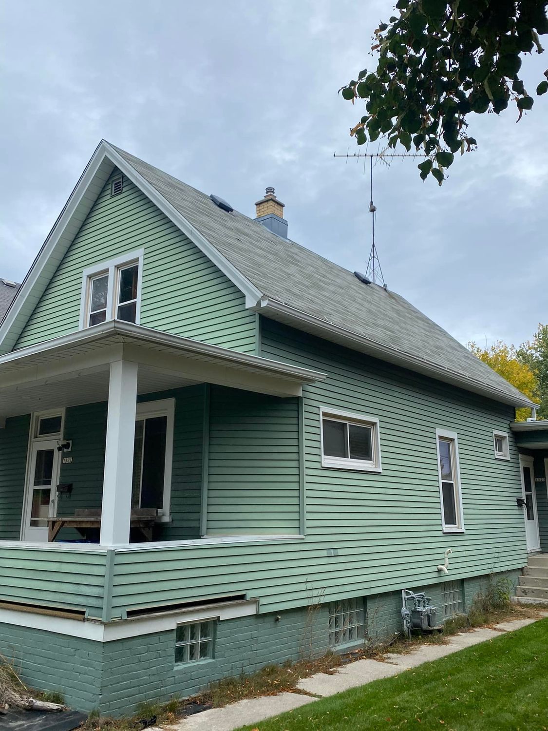 Mint-green house with white trim and porch, viewed from the side under a cloudy sky.