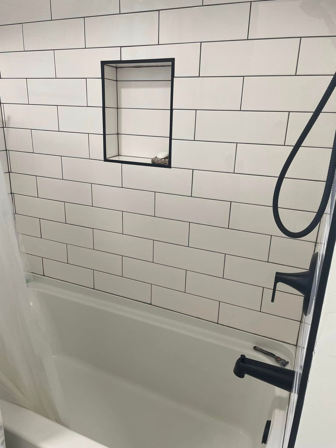 White-tiled shower/tub with black fixtures and a small recessed niche above the tub