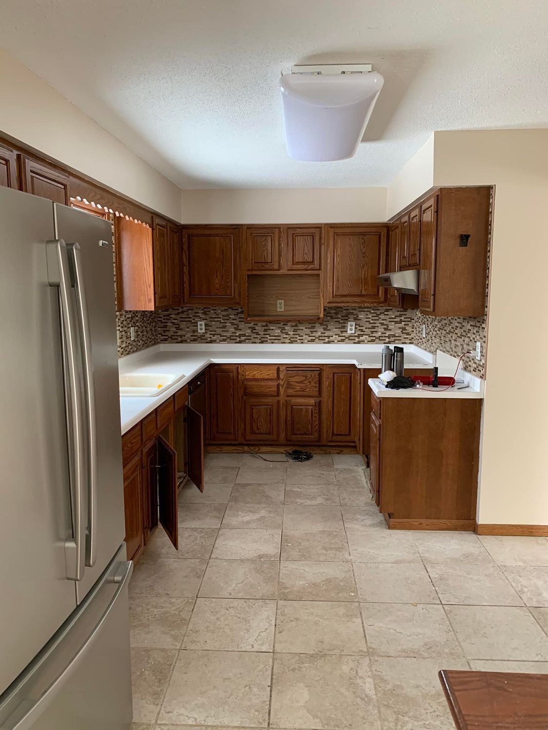 Small kitchen with stainless steel fridge, wooden cabinets, beige tile floor, and a skylight.