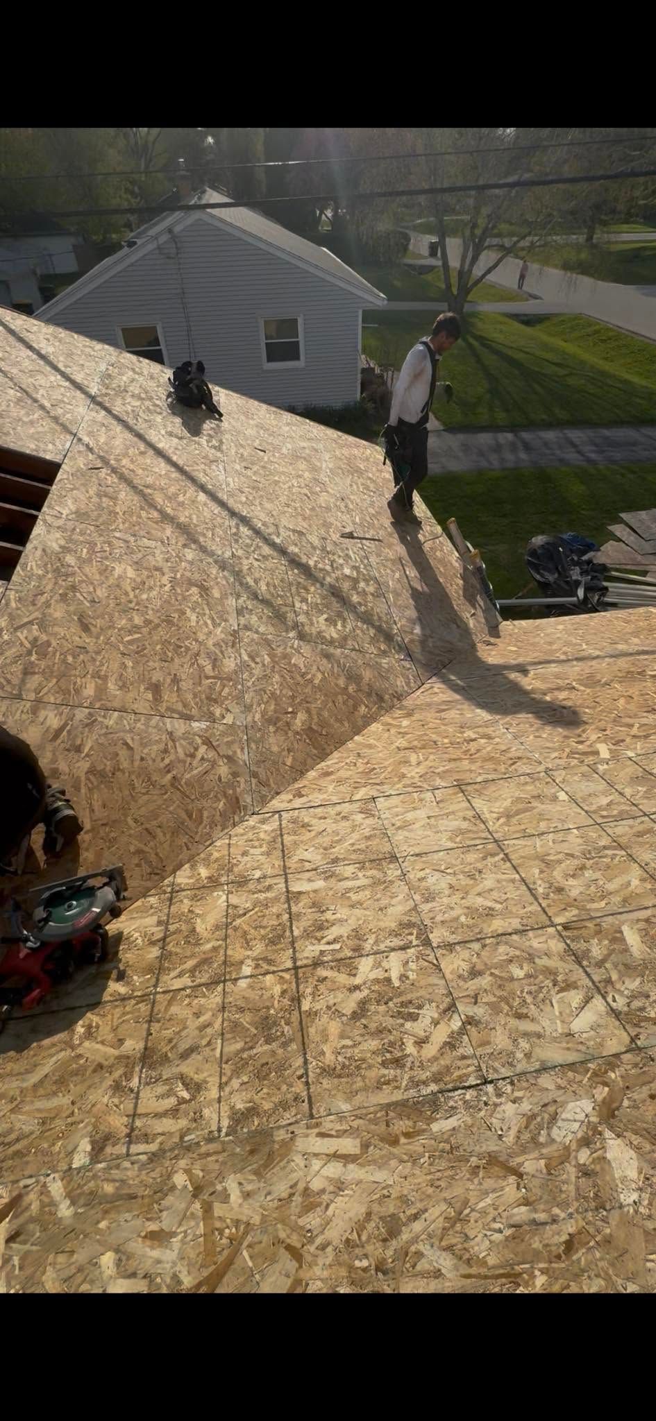 Workers roofing a house with plywood sheets in bright sunlight.