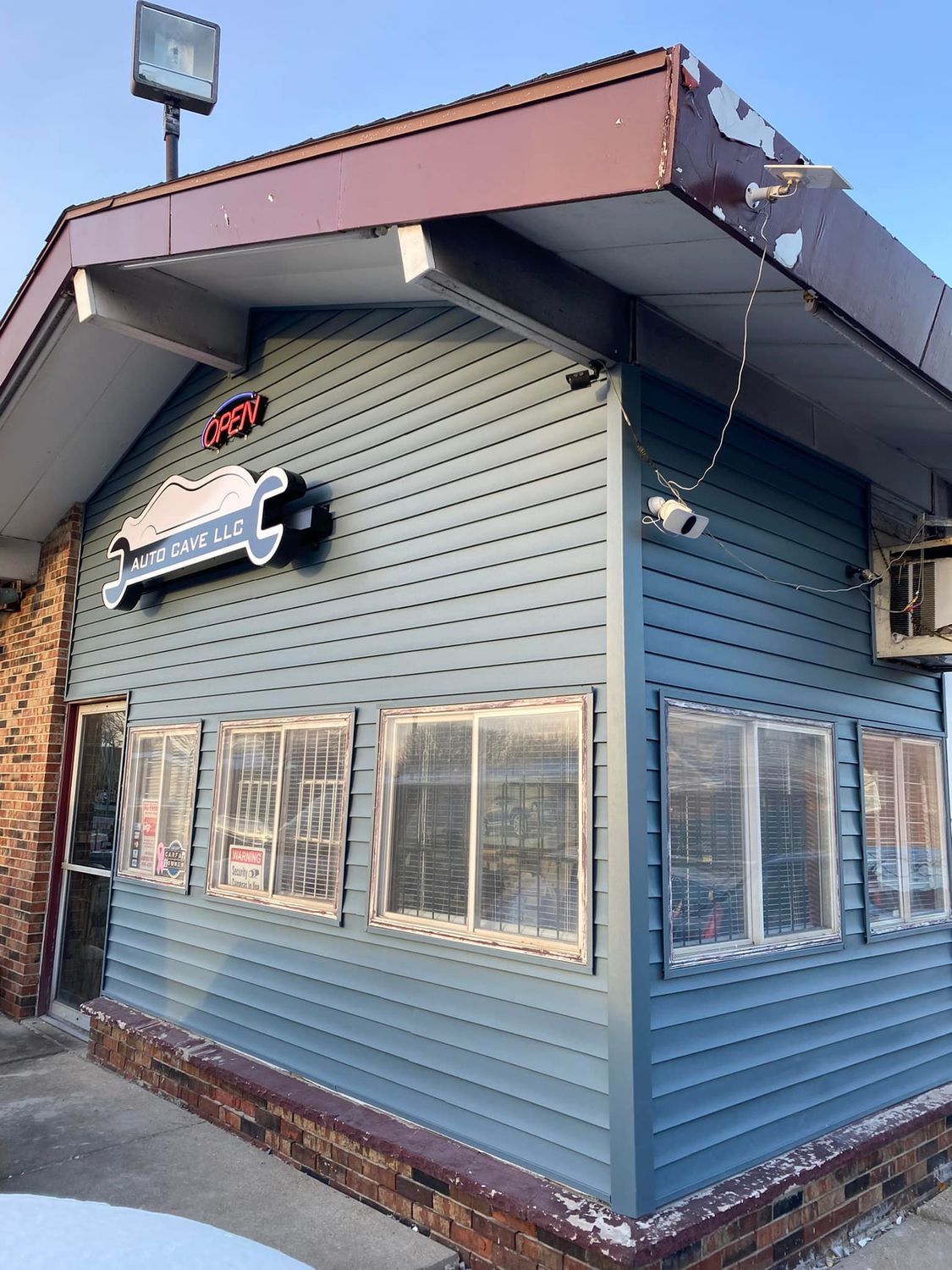 Small blue corner storefront with a red roof, windows, and a hanging sign on the side.