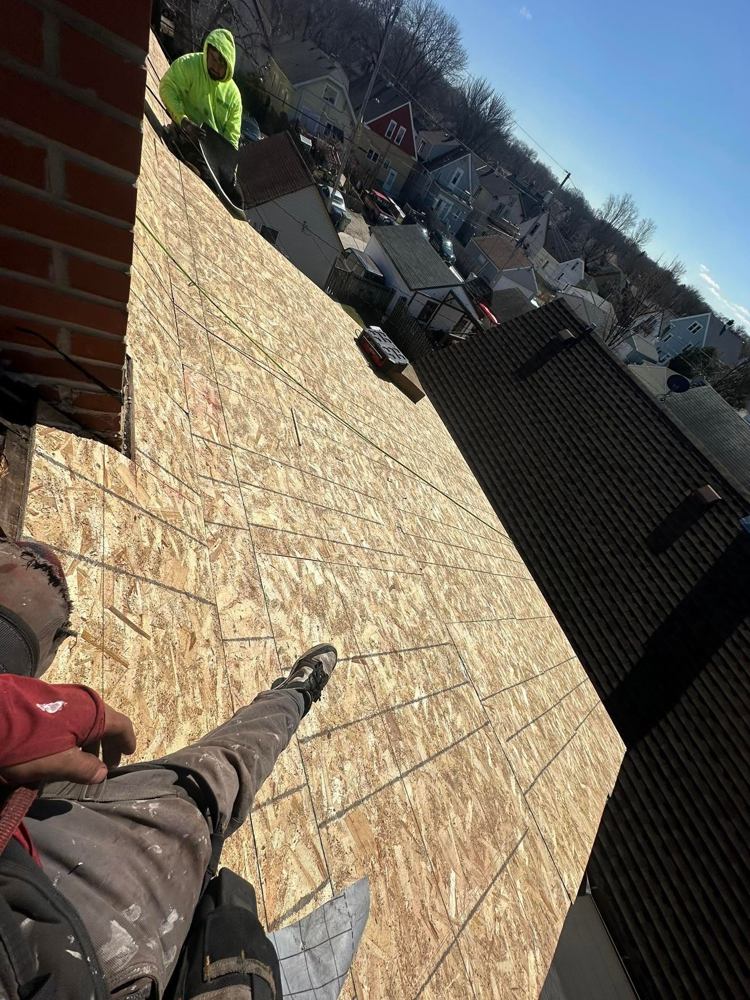 Rooftop terrace with a person standing near the edge, overlooking houses and a bright blue sky.