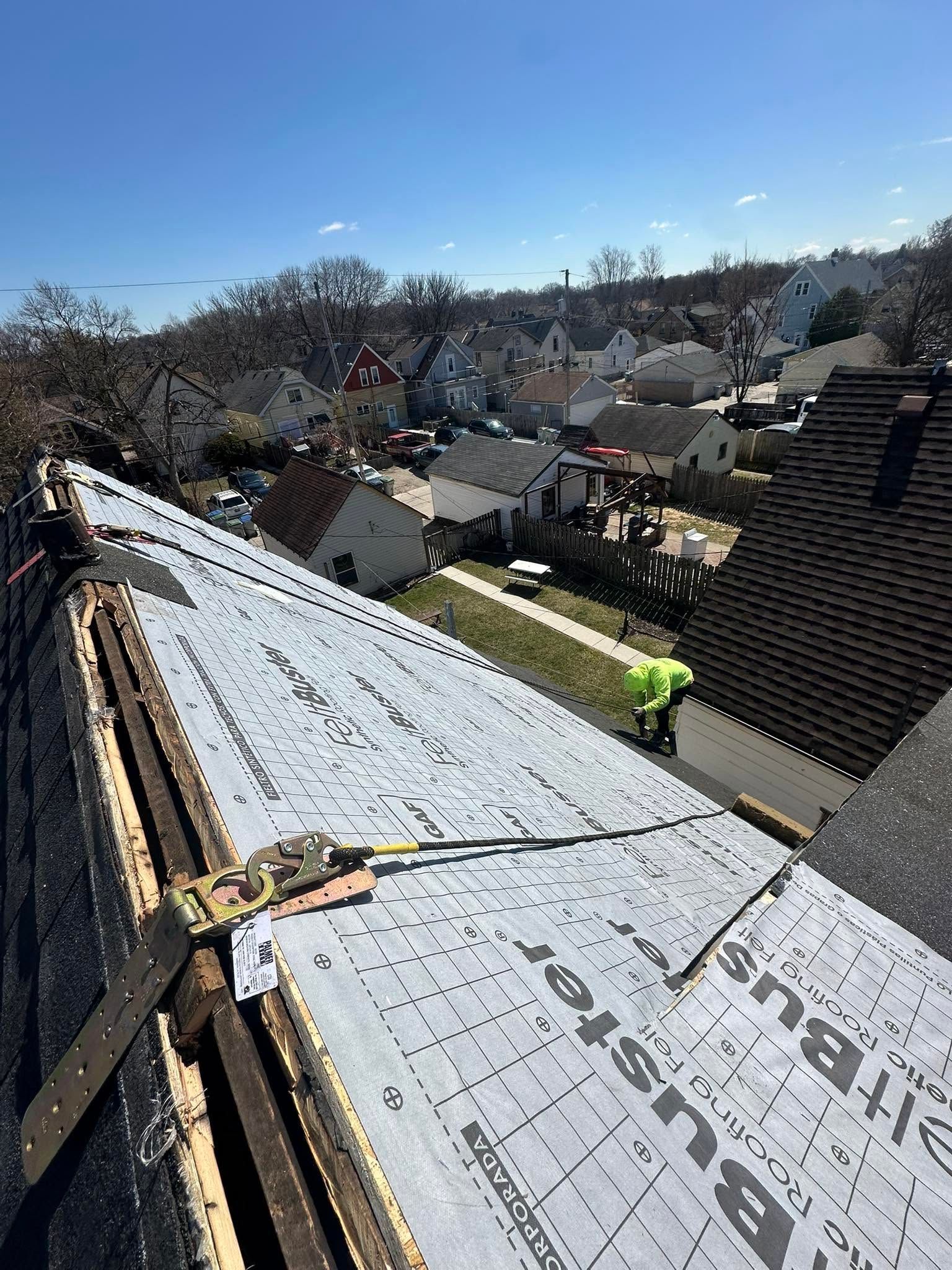 Roof under construction with gray underlayment overlooking a residential neighborhood on a sunny day