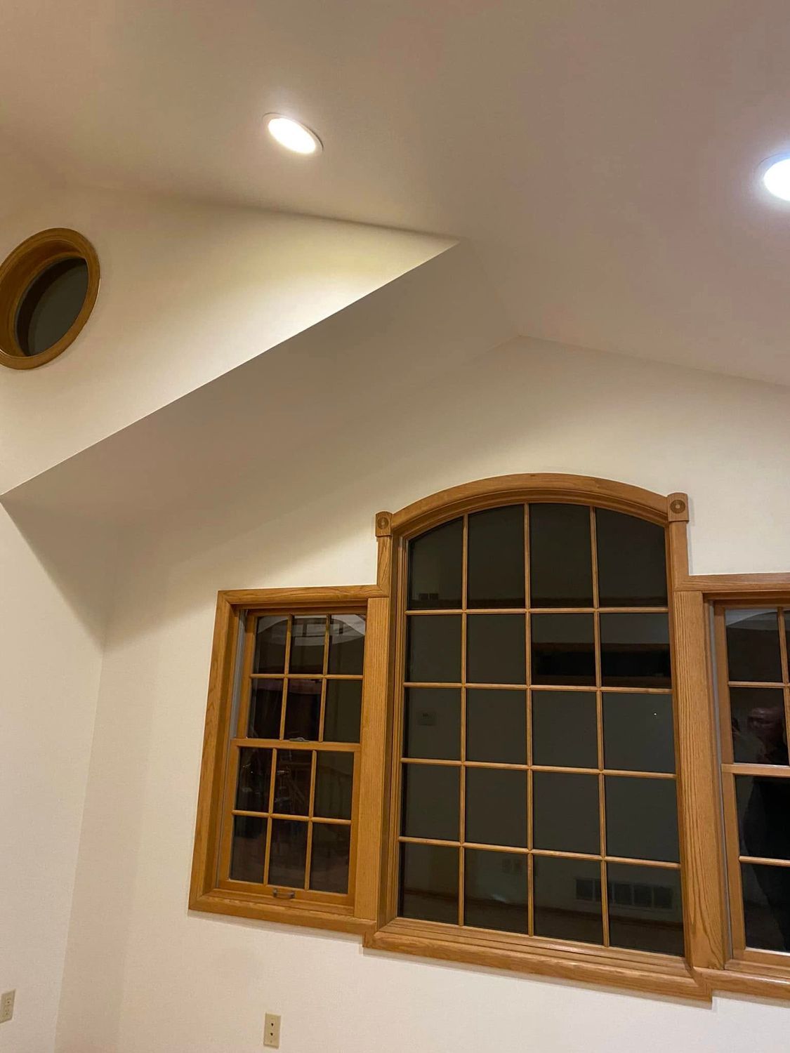 Interior wall with wooden-trimmed arched windows and recessed ceiling lights.