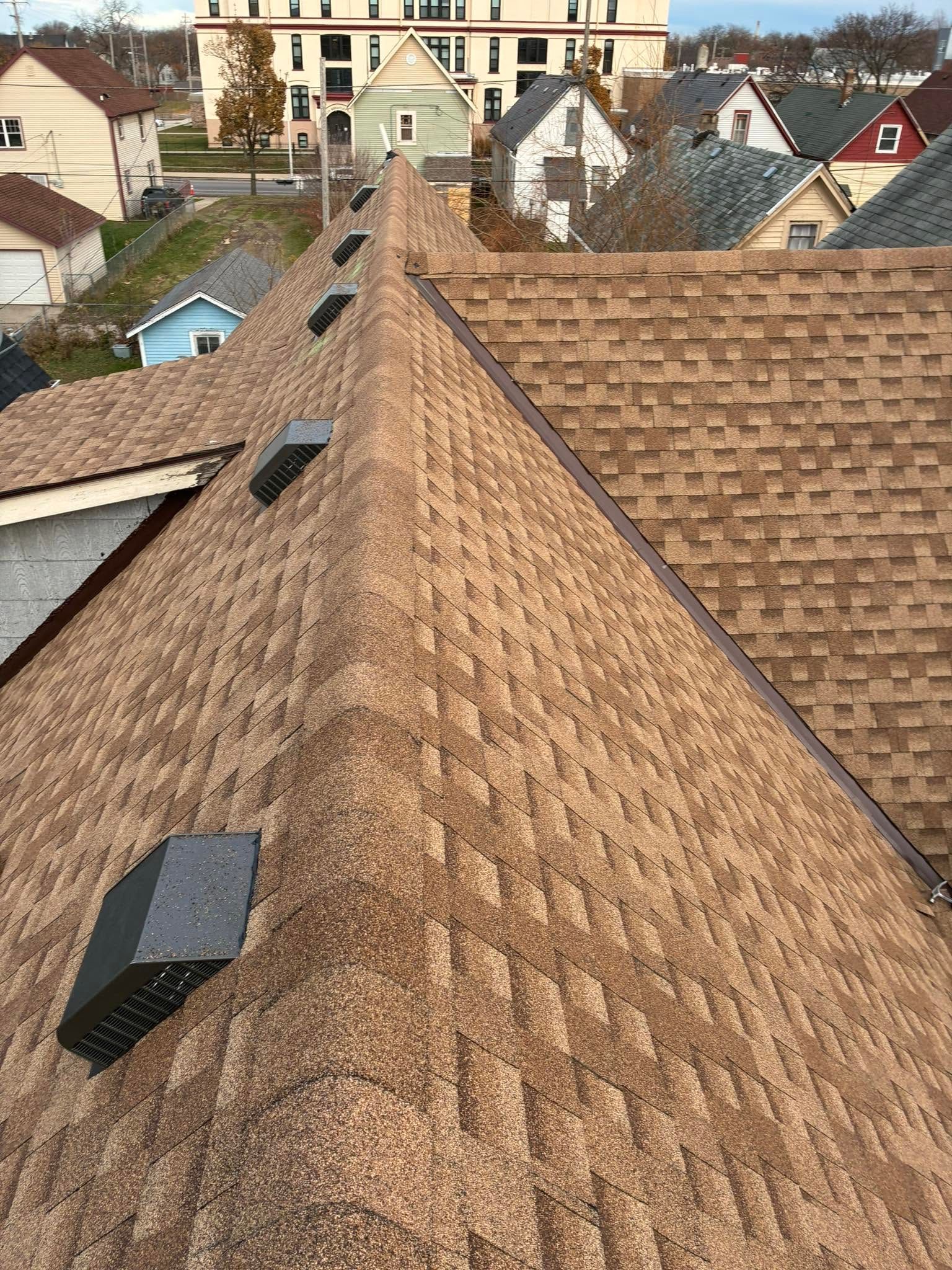 Aerial view of a brown shingled roof with skylights in a residential neighborhood
