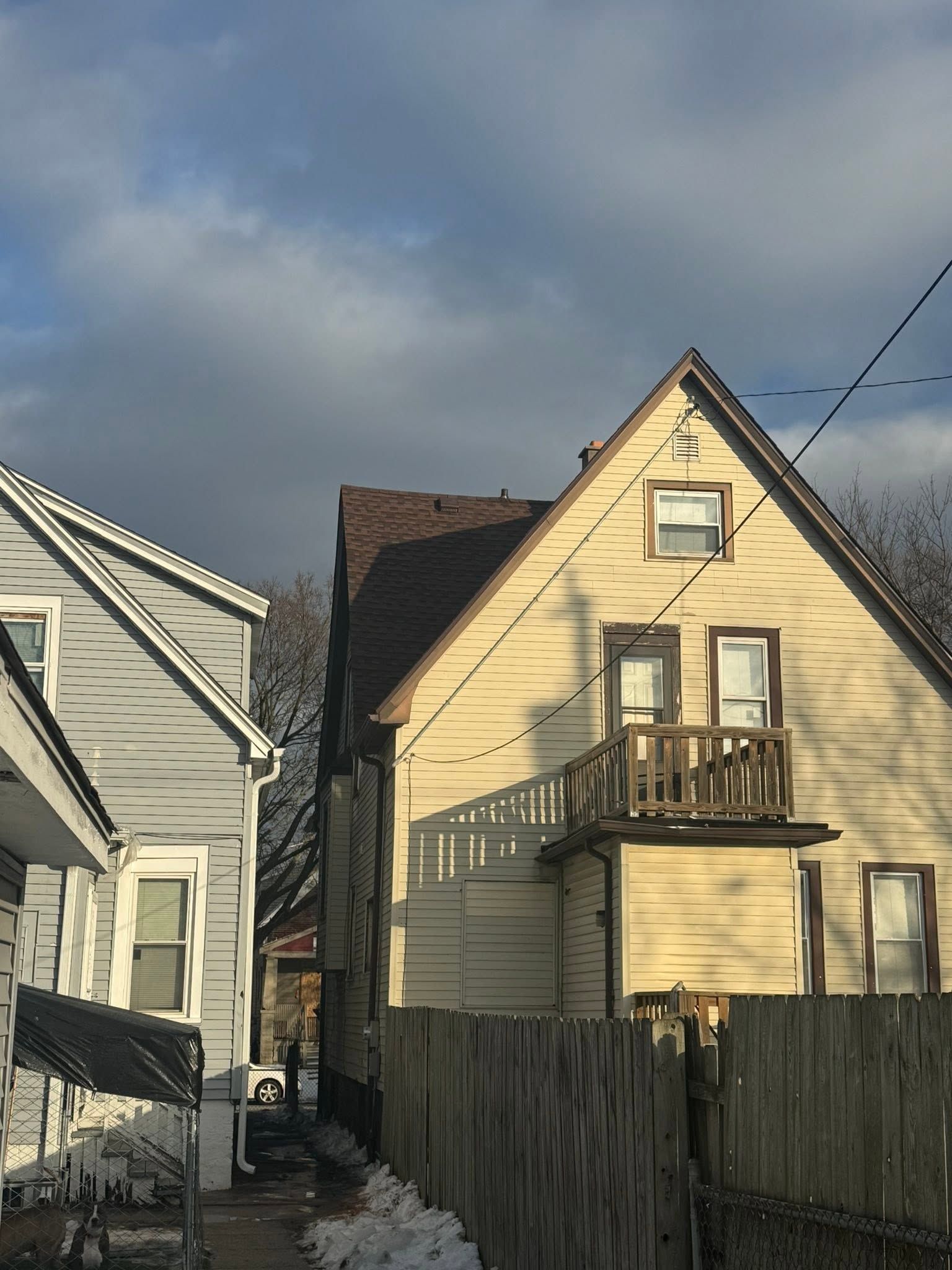 Two narrow houses with weathered siding and fenced yards under a cloudy sky