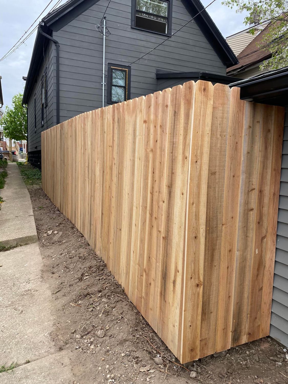 Wooden privacy fence along a narrow side yard beside a gray house and concrete walkway