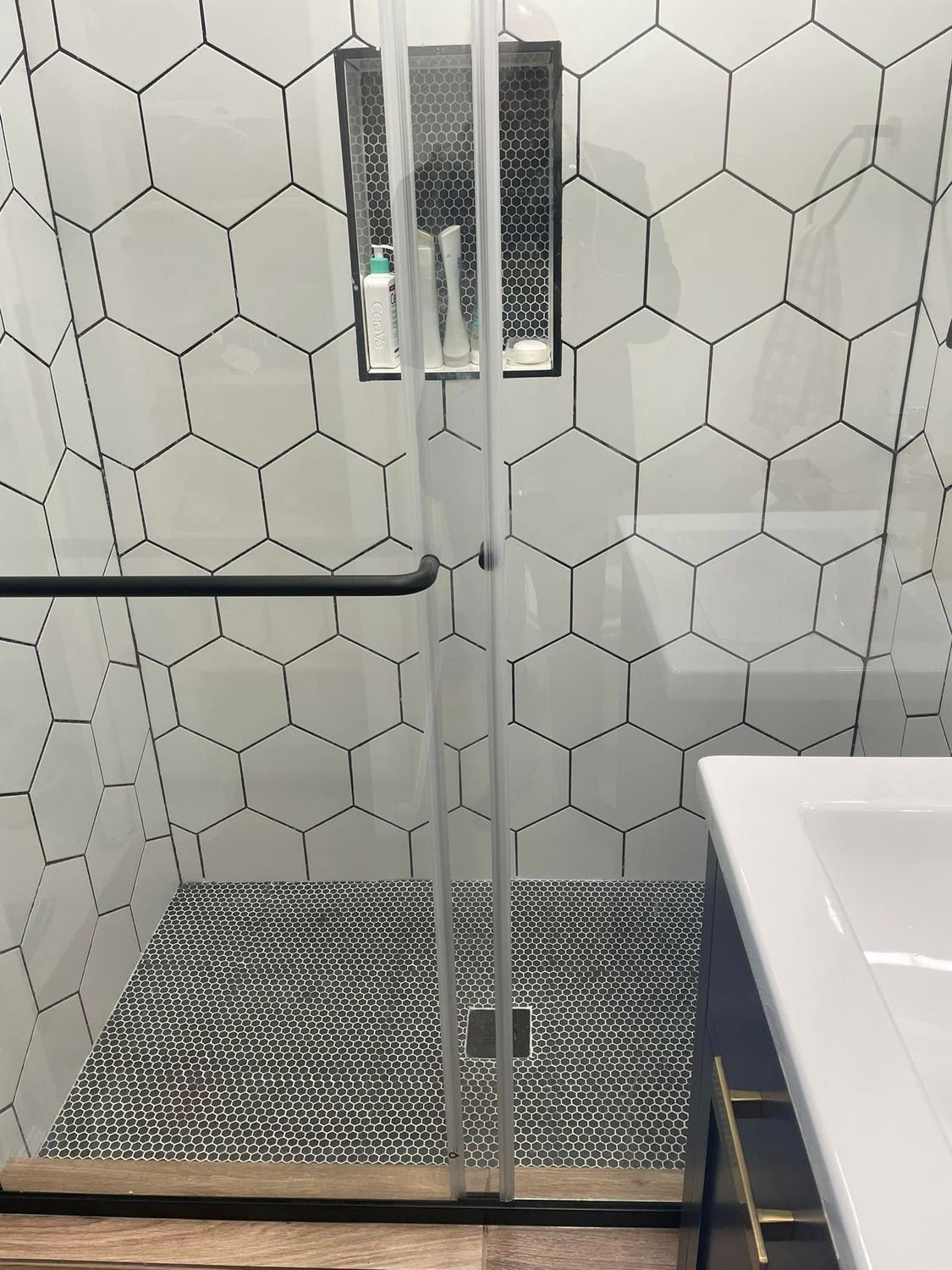 Modern shower with glass doors, hexagon tile walls, and a white sink at right