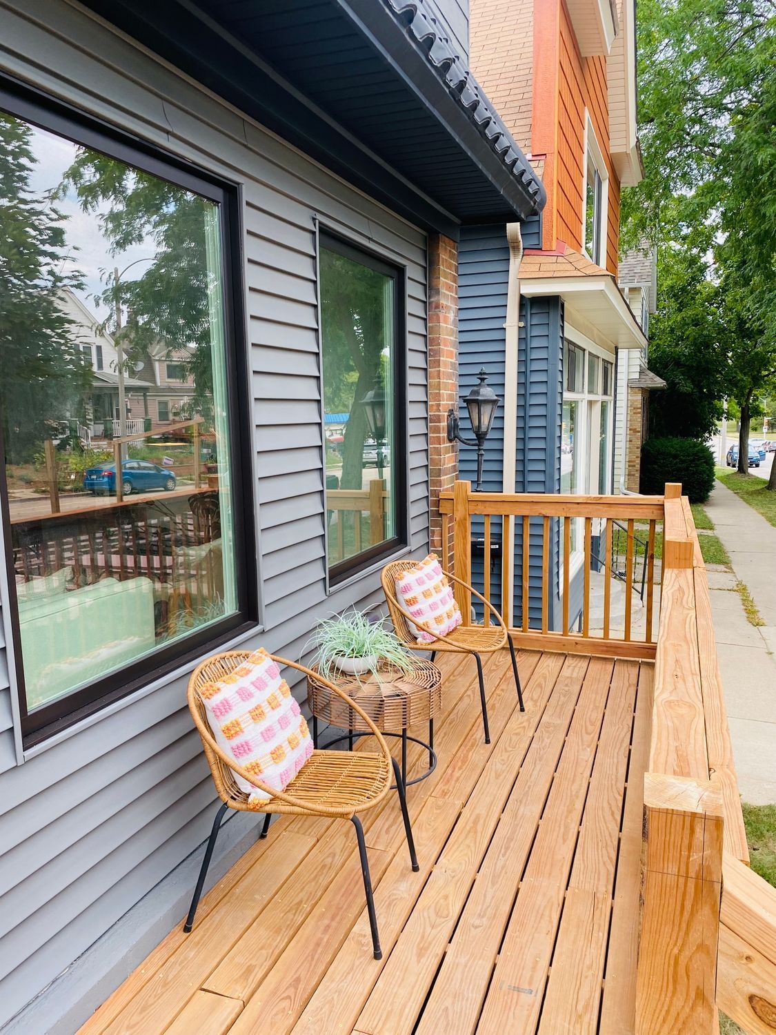 Small wooden porch with two patterned chairs beside gray siding and large windows outdoors.