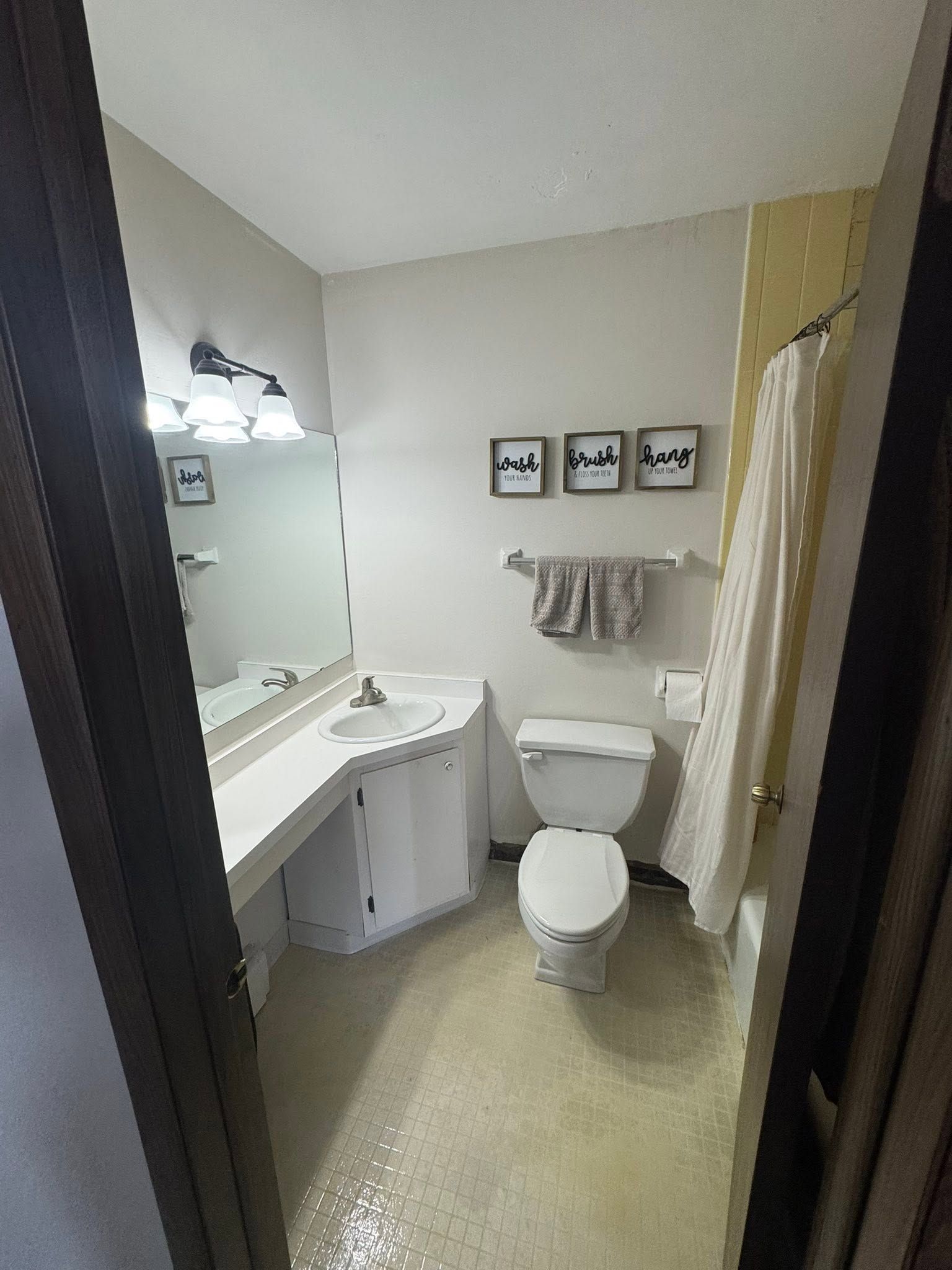 Small bathroom with a sink, toilet, mirror, towel rack, and framed wall art