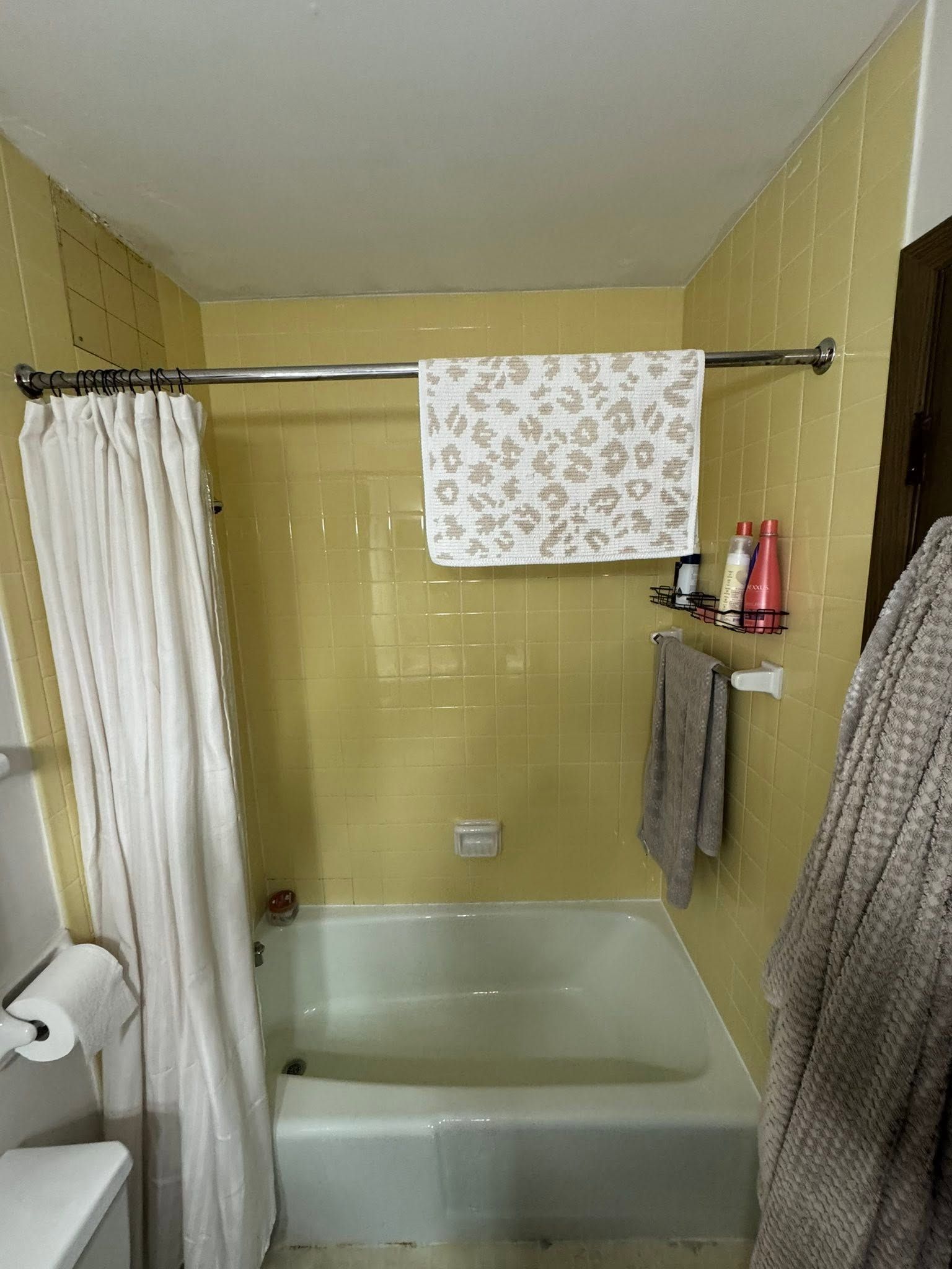 Small beige bathroom with a shower-tub, white curtain, towel bar, and towels hanging over the tub.