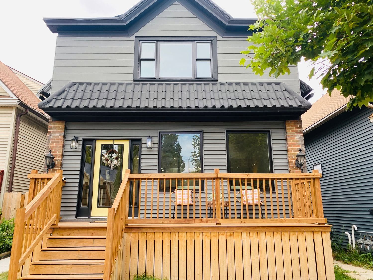 Two-story gray house with black roof and wooden front porch and steps