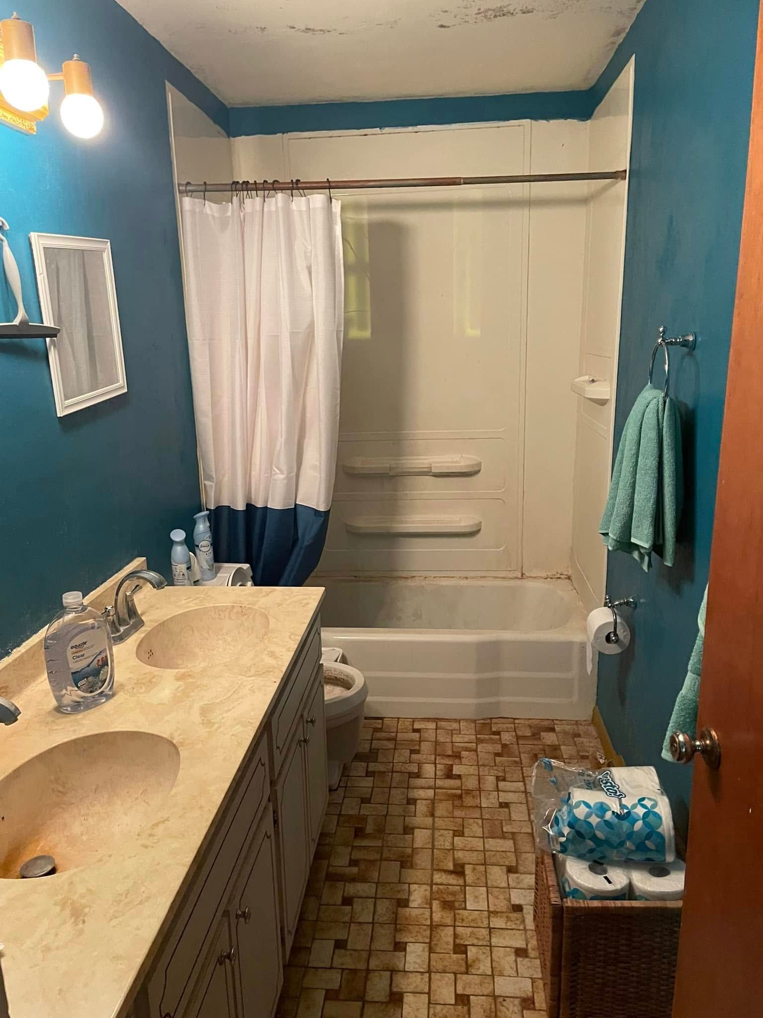 Small bathroom with teal walls, white tub and shower curtain, beige vanity, and patterned floor tiles.