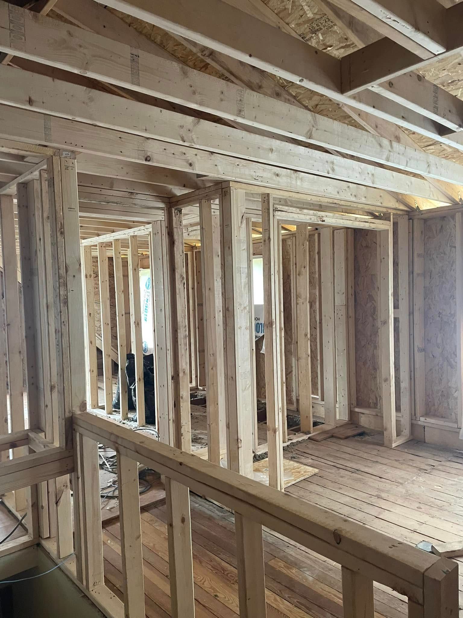 Unfinished wooden interior framing with exposed beams, studs, and a partially built staircase area.