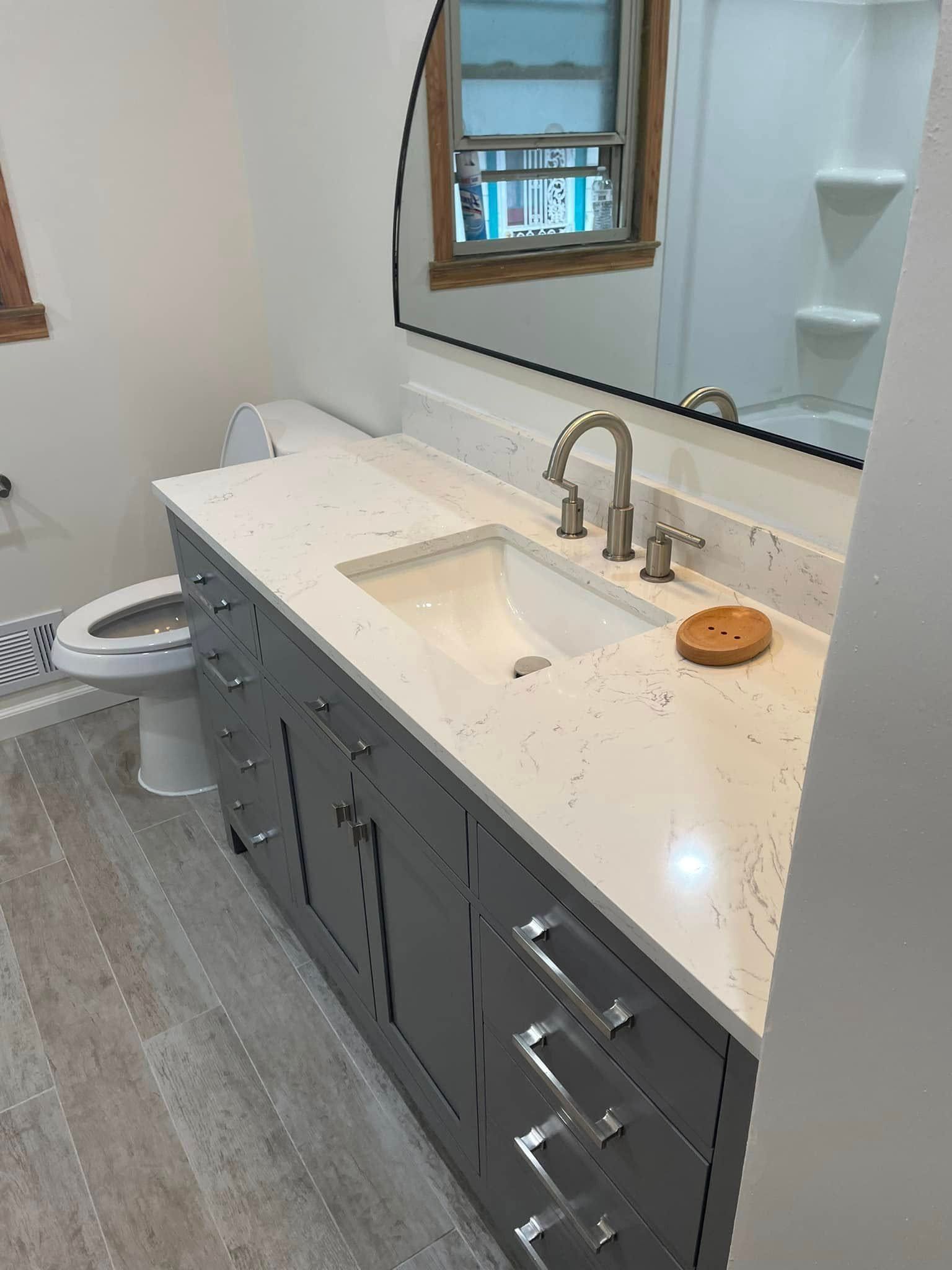 Bathroom vanity with gray cabinets, white countertop, sink, mirror, and chrome faucet.
