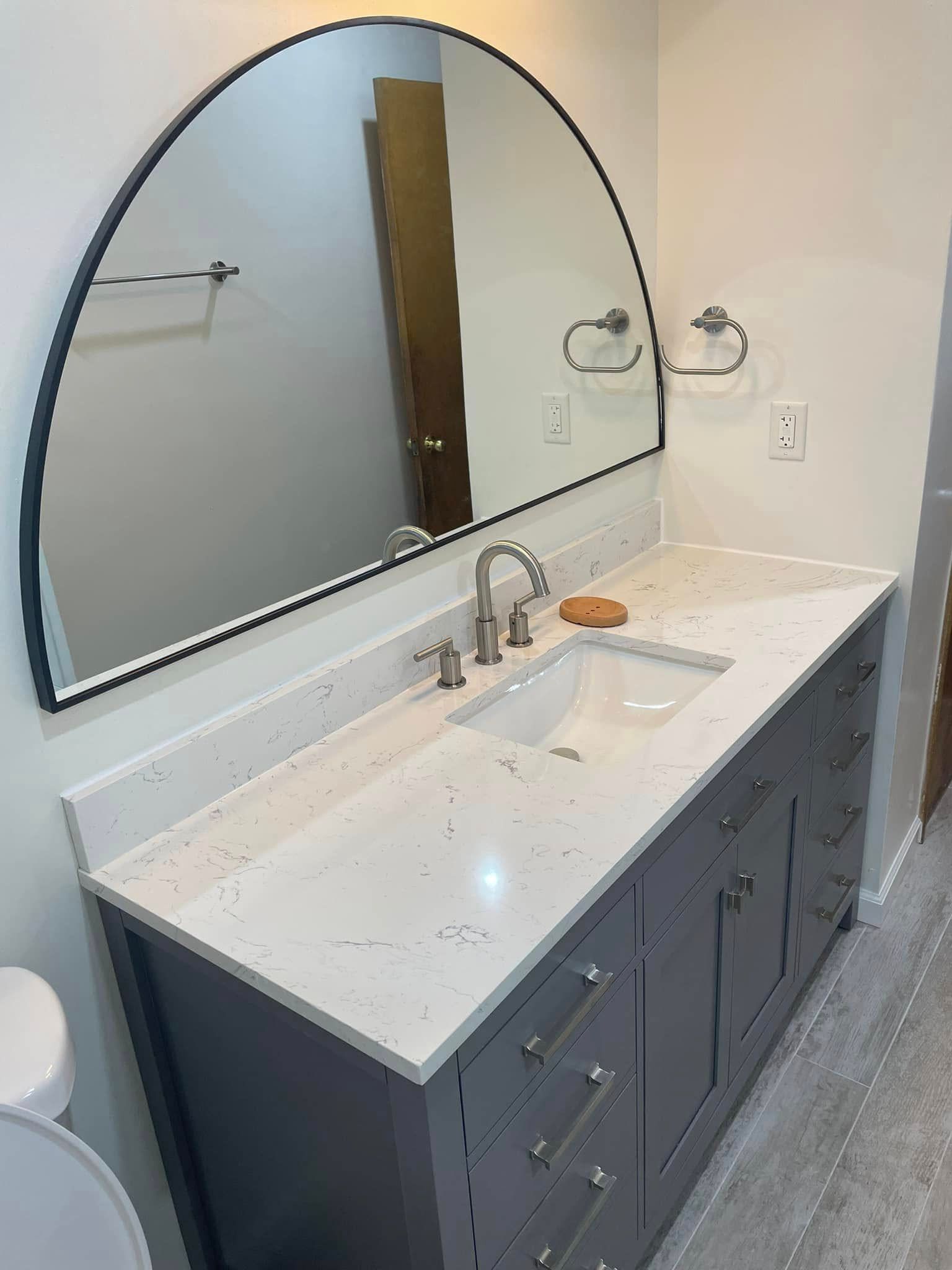 Modern bathroom vanity with large arched mirror, white countertop, and dark blue cabinets