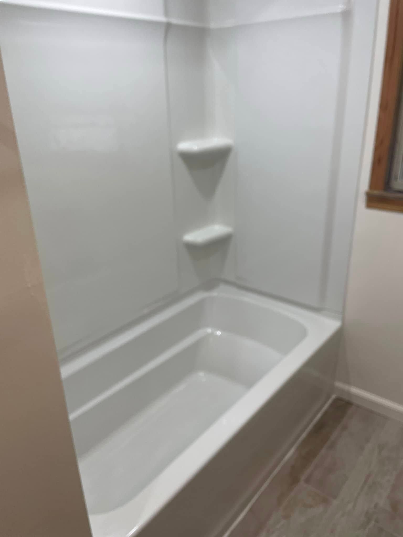 White bathtub with built-in corner shelves and light wood flooring in a small bathroom