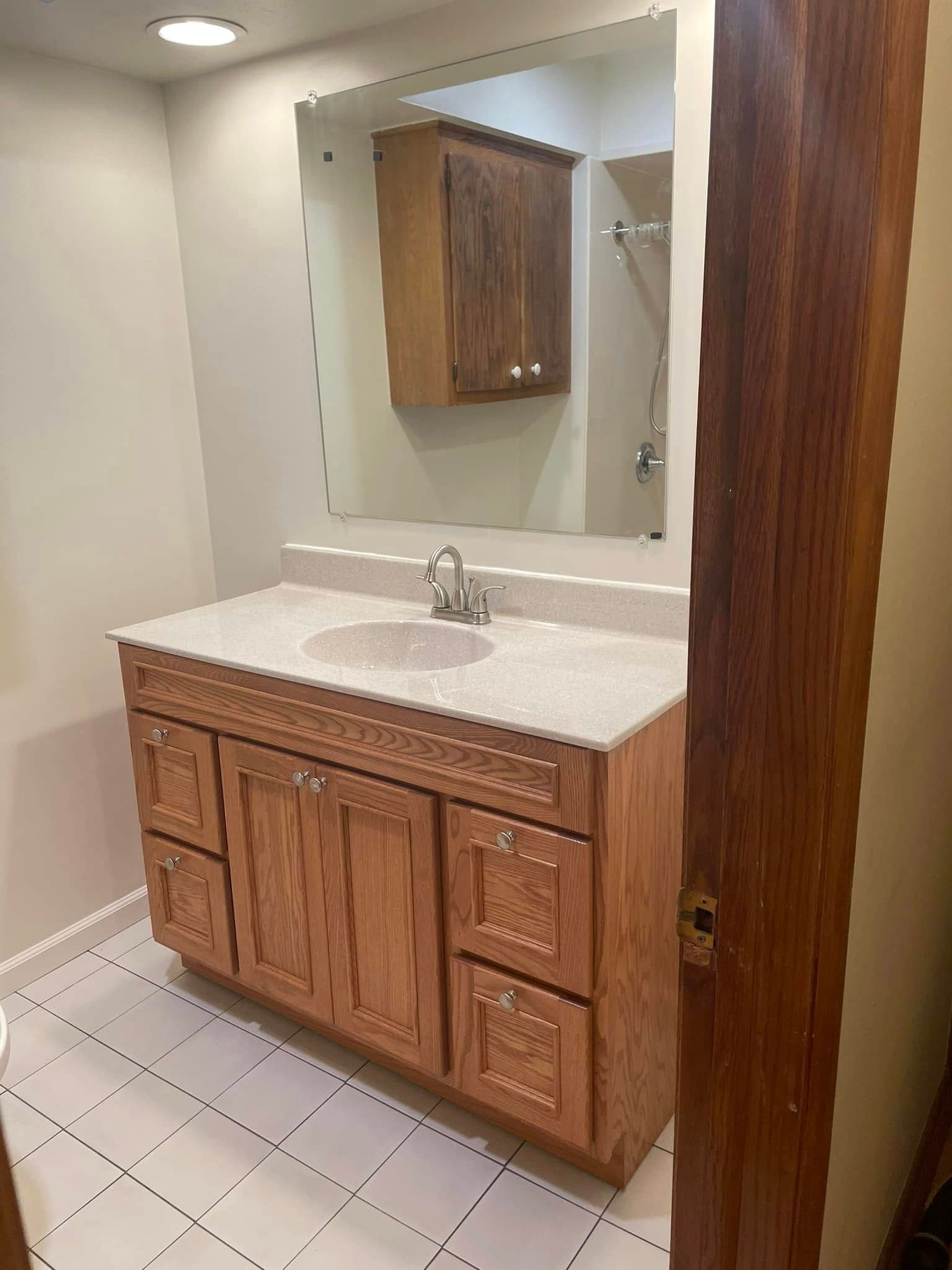 Small bathroom vanity with wood cabinets, white countertop, mirror, and tile floor in a narrow space