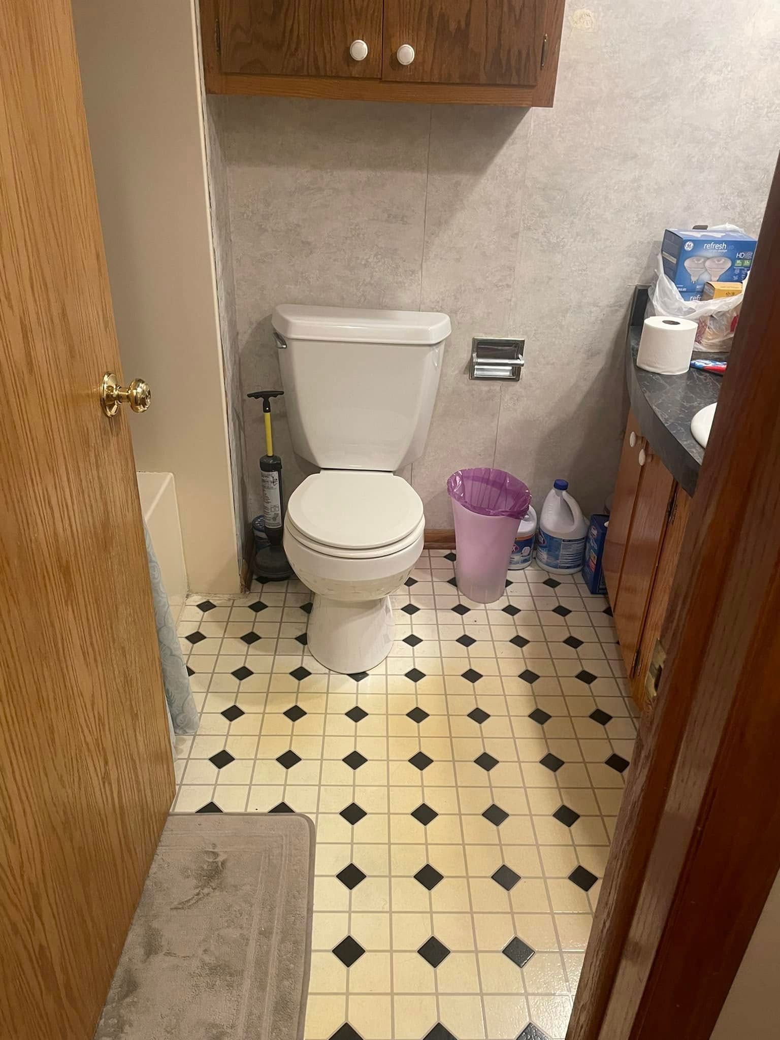 Small bathroom with a toilet, beige patterned tile floor, and a purple wastebasket beside the sink.