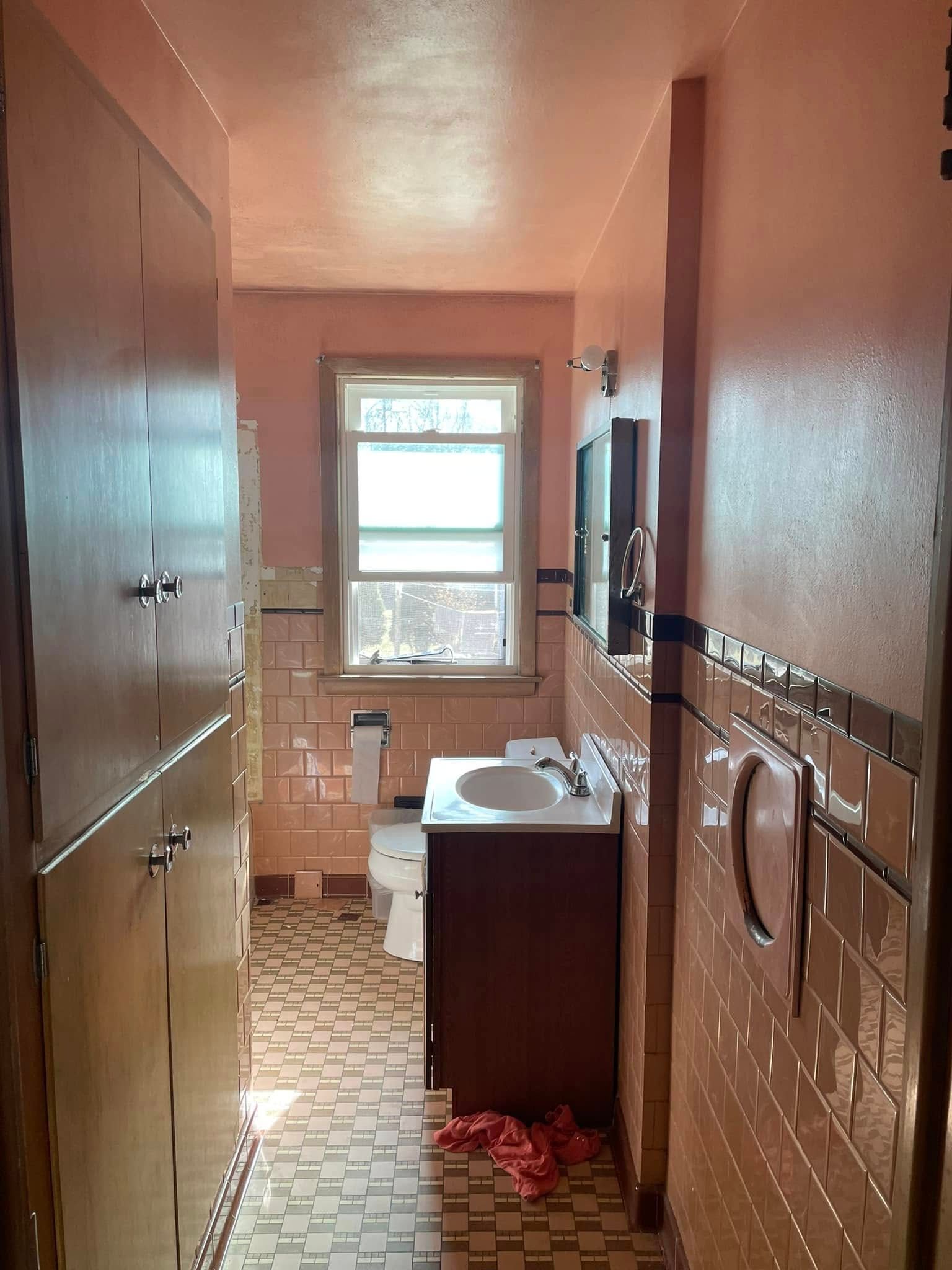 Narrow bathroom hallway with a sink vanity, tiled walls, and a window at the far end.