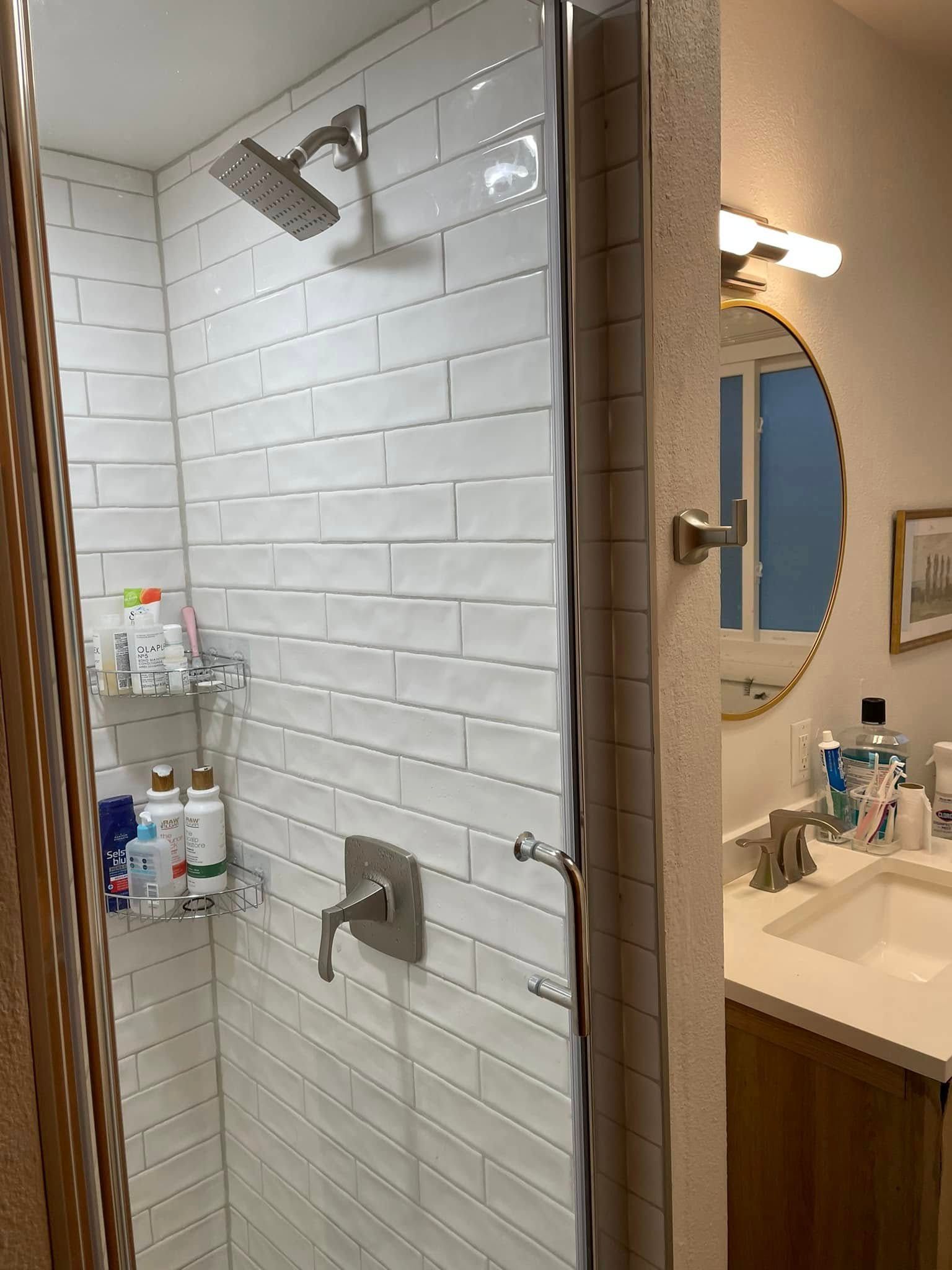 White-tiled shower with grab bars, built-in shelves, and a bathroom sink visible beside it.