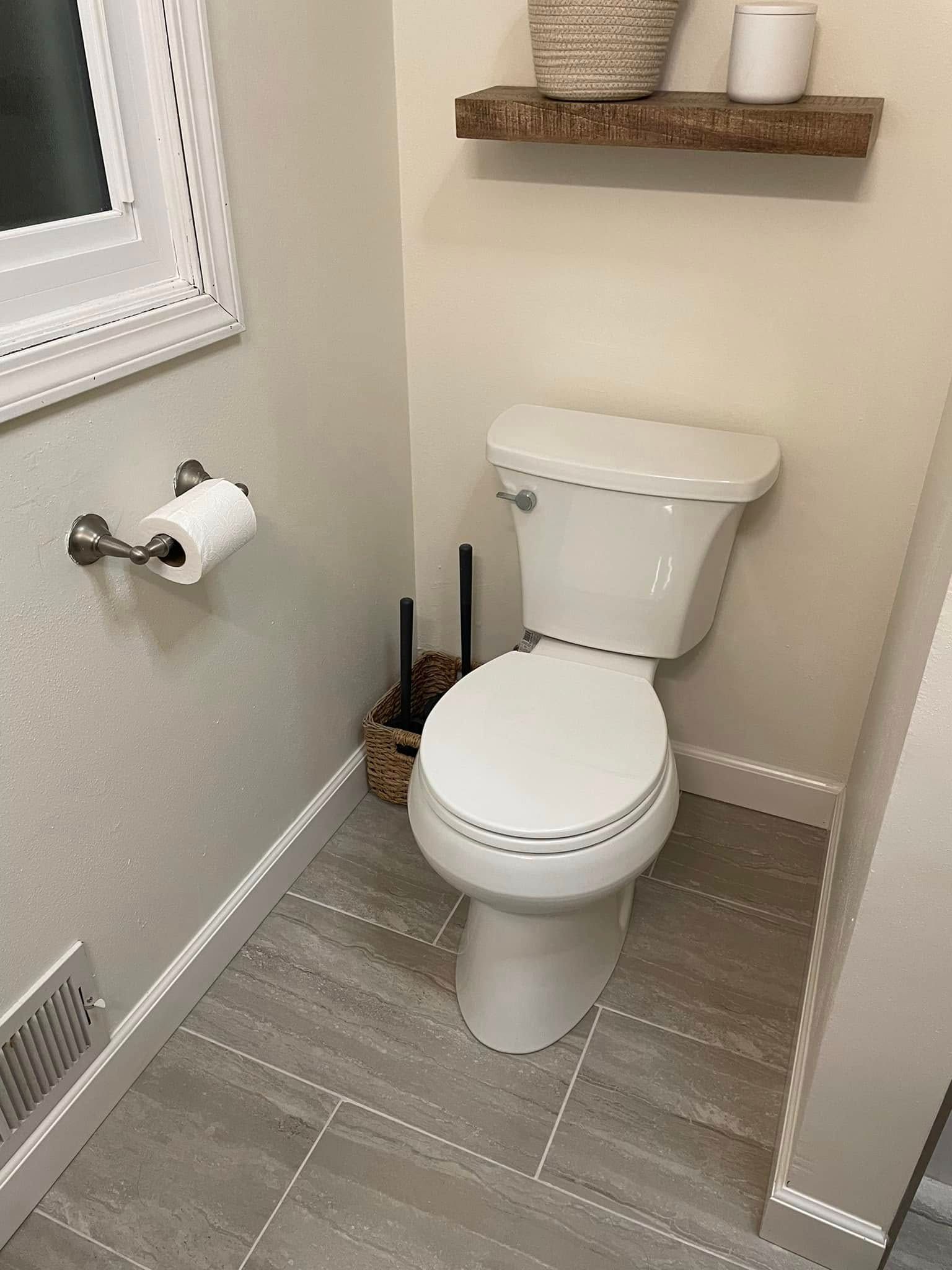 Small bathroom with a white toilet, gray tile floor, and a wall shelf above it.