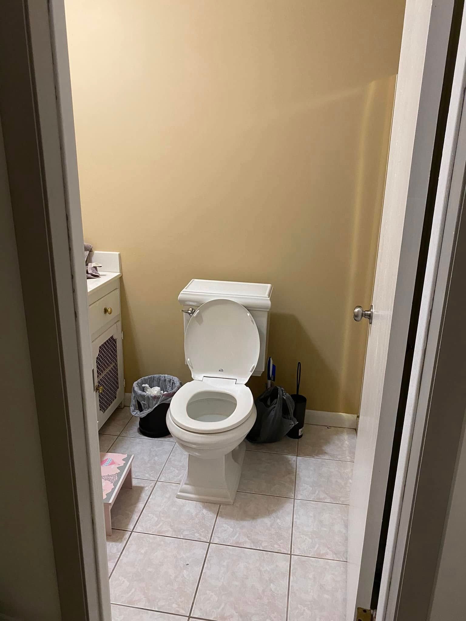 Small bathroom with a toilet centered between a cabinet and cleaning tools on tiled floor.