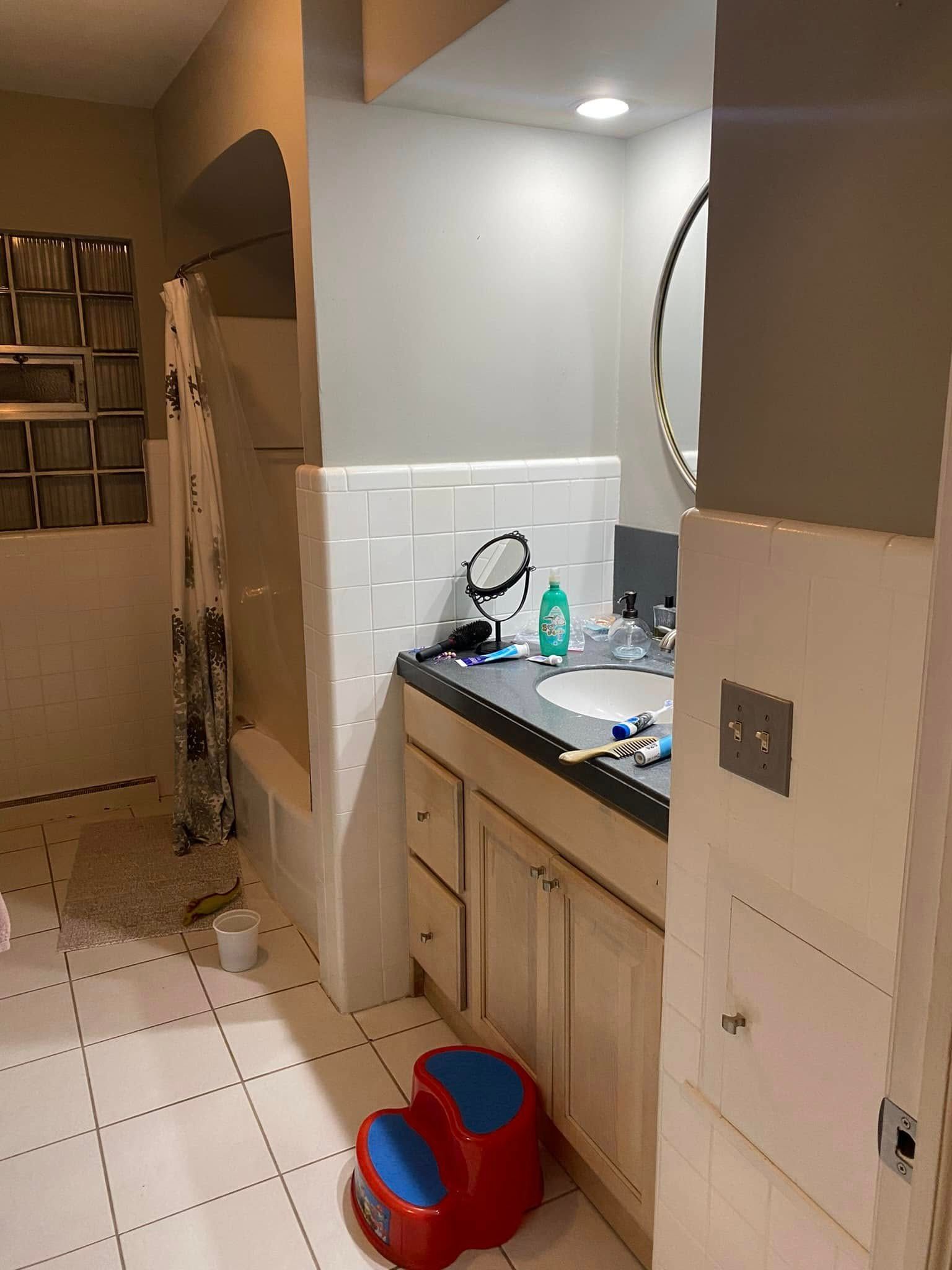 Bathroom vanity with sink and mirror, tiled floor, and a red-and-blue child’s toy on the floor