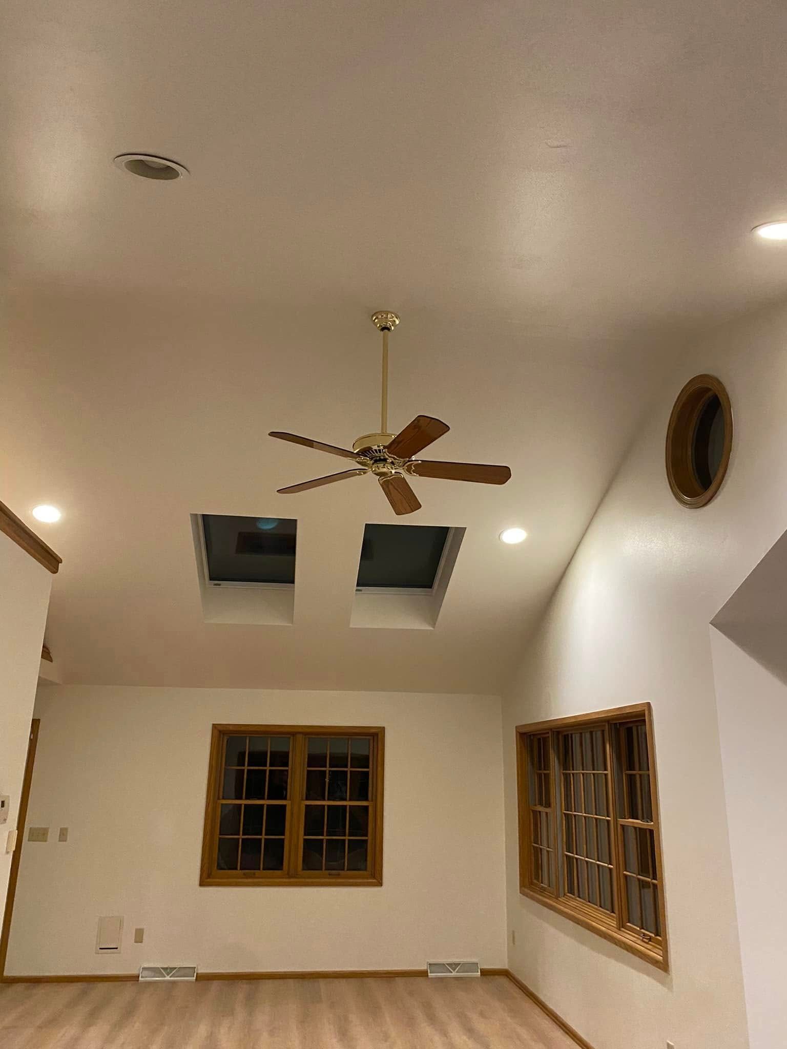 Empty living room with vaulted white ceiling, ceiling fan, recessed lights, windows, and a skylight.