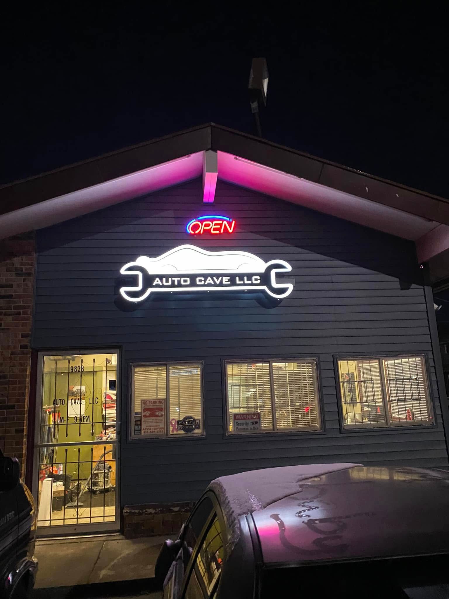 Night view of a neon-lit auto repair shop with a glowing sign and parked car in front.