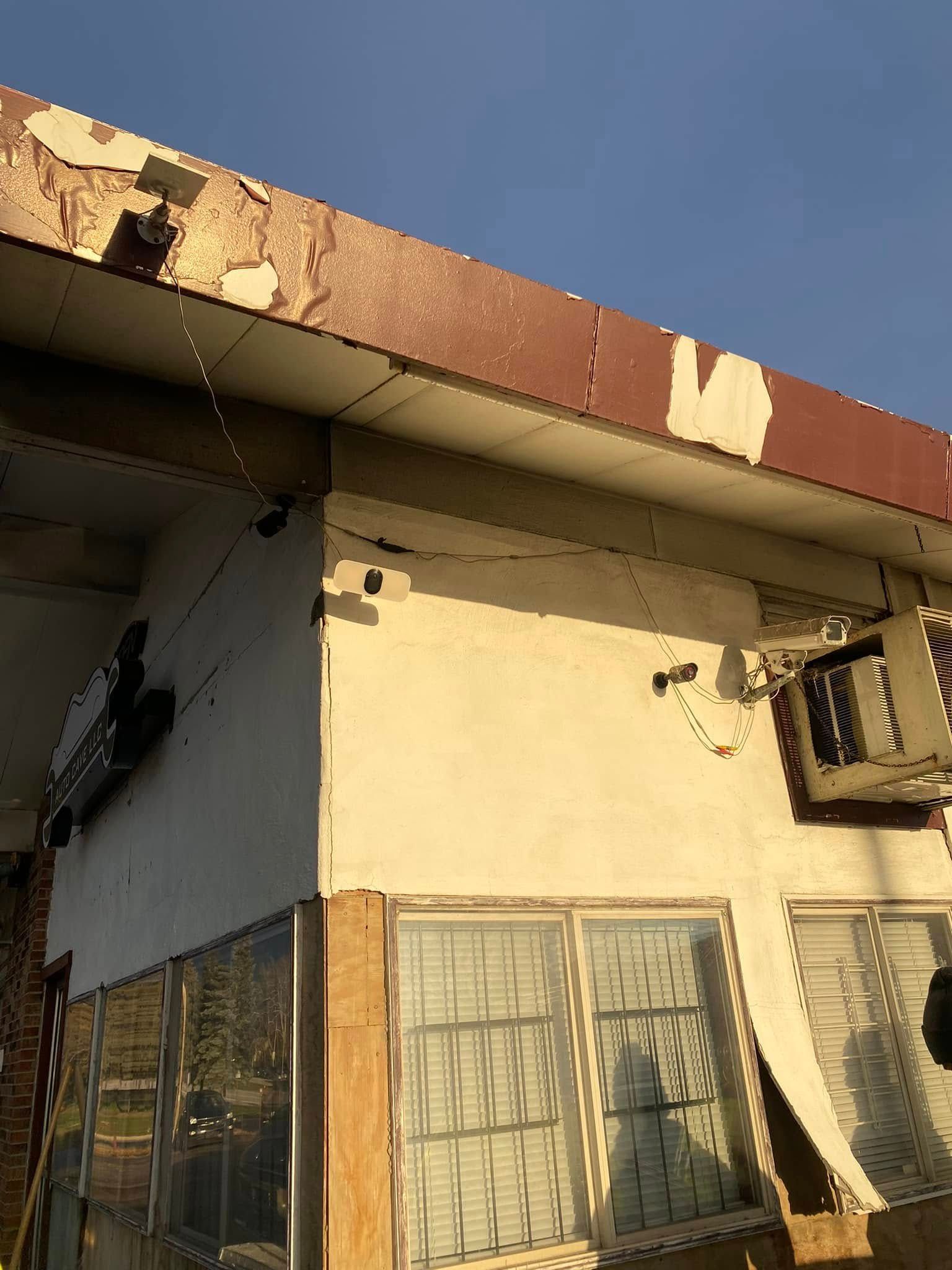 Weathered cream building with peeling paint, rusted roof edge, barred windows, and a clear blue sky.