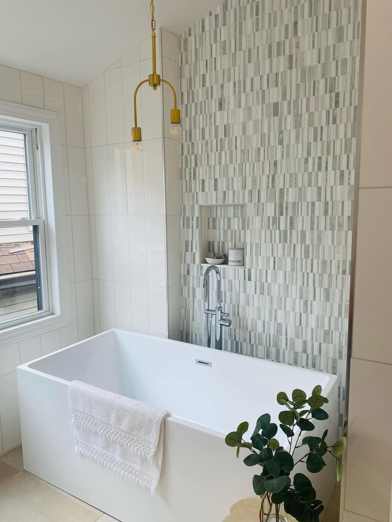 Modern bathroom with freestanding tub, brass shower, mosaic accent wall, and towel.