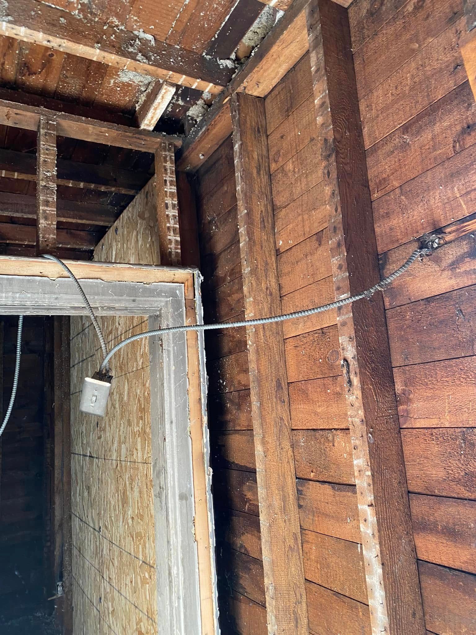 Damaged interior wall with exposed wood framing and a hanging electrical wire in a partially renovated room