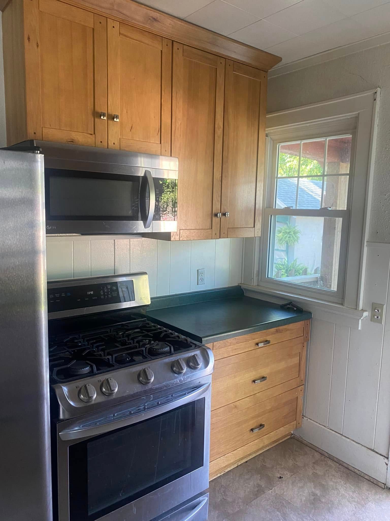 Small kitchen with wooden cabinets, stainless steel stove, dark countertop, and a window letting in daylight