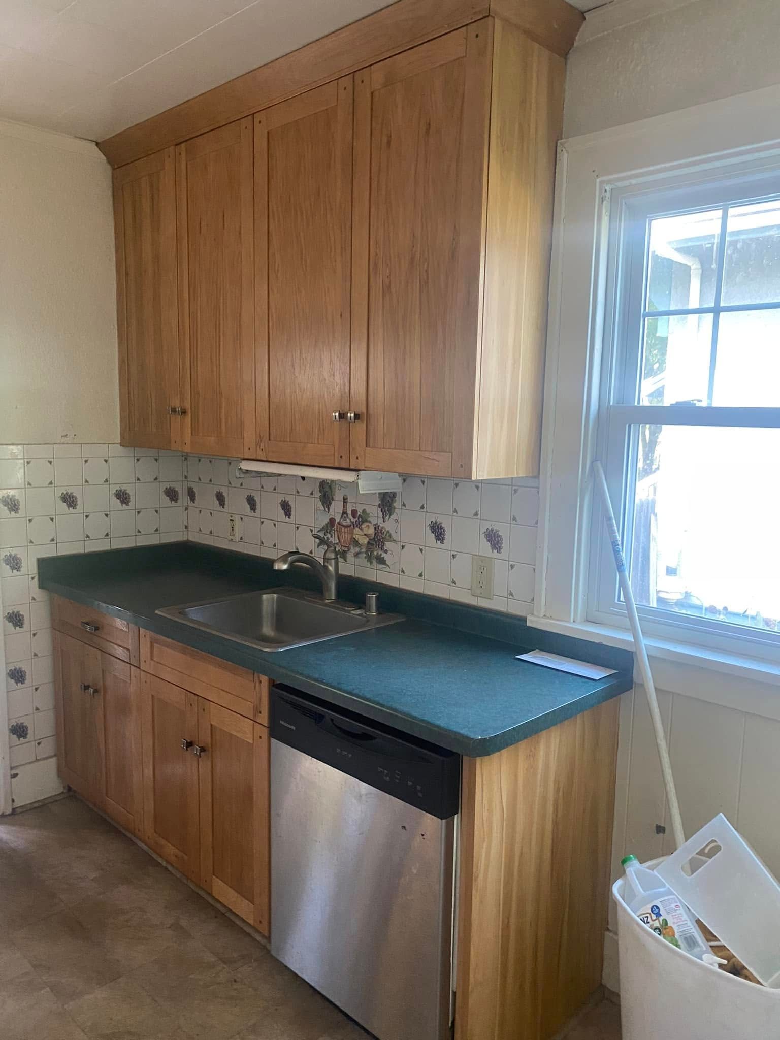 Kitchen with wood cabinets, dark countertop, stainless dishwasher, and window over the sink.