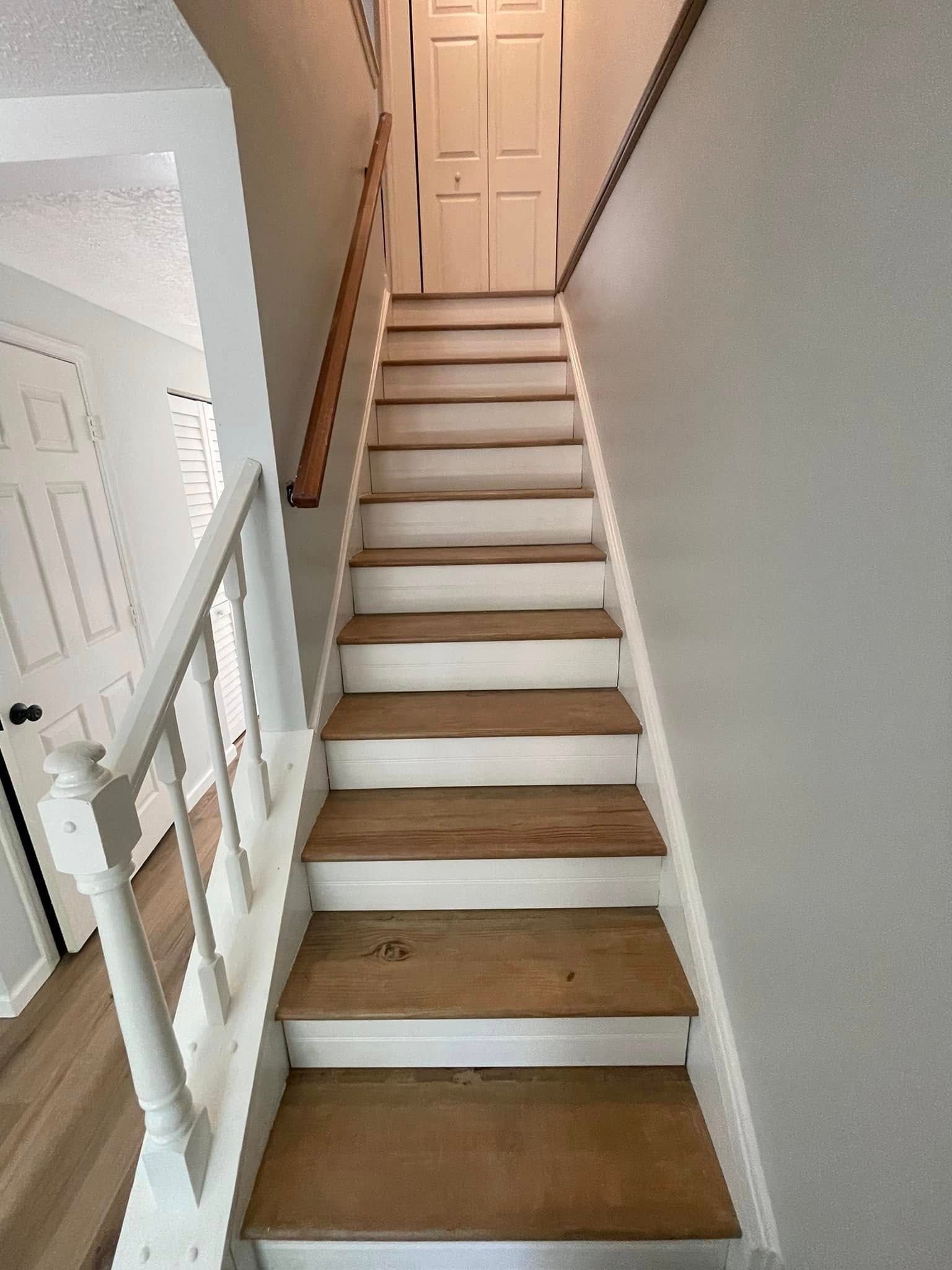 Narrow indoor staircase with white railings and wooden steps leading to a closed door.