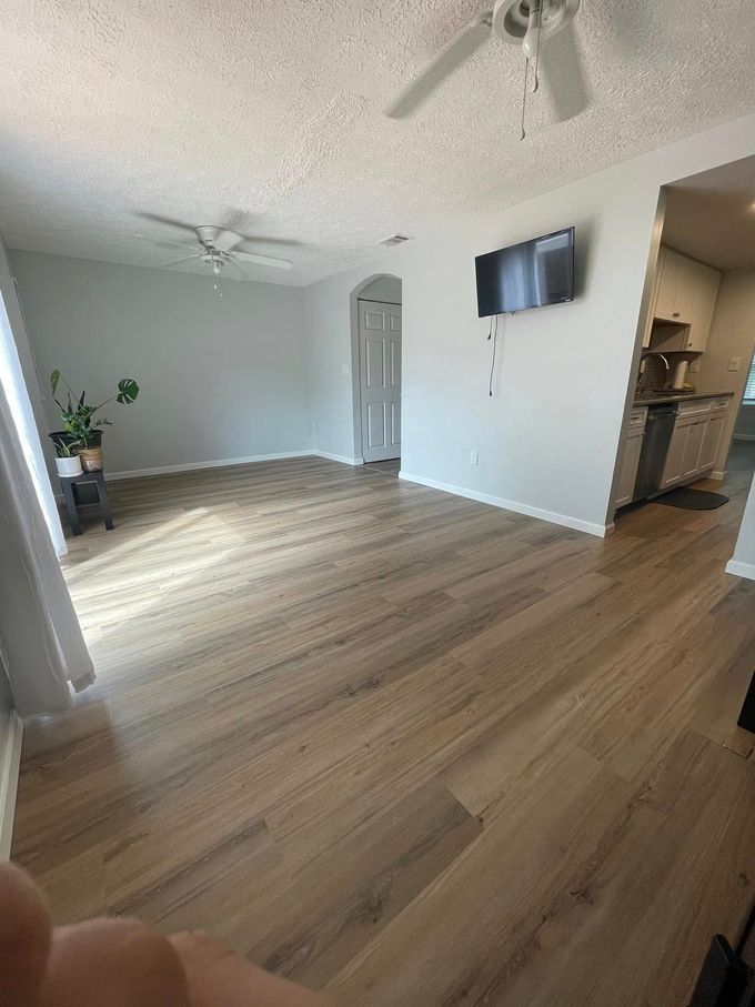 Spacious empty living room with wood floors, gray walls, ceiling fans, and a wall-mounted TV.