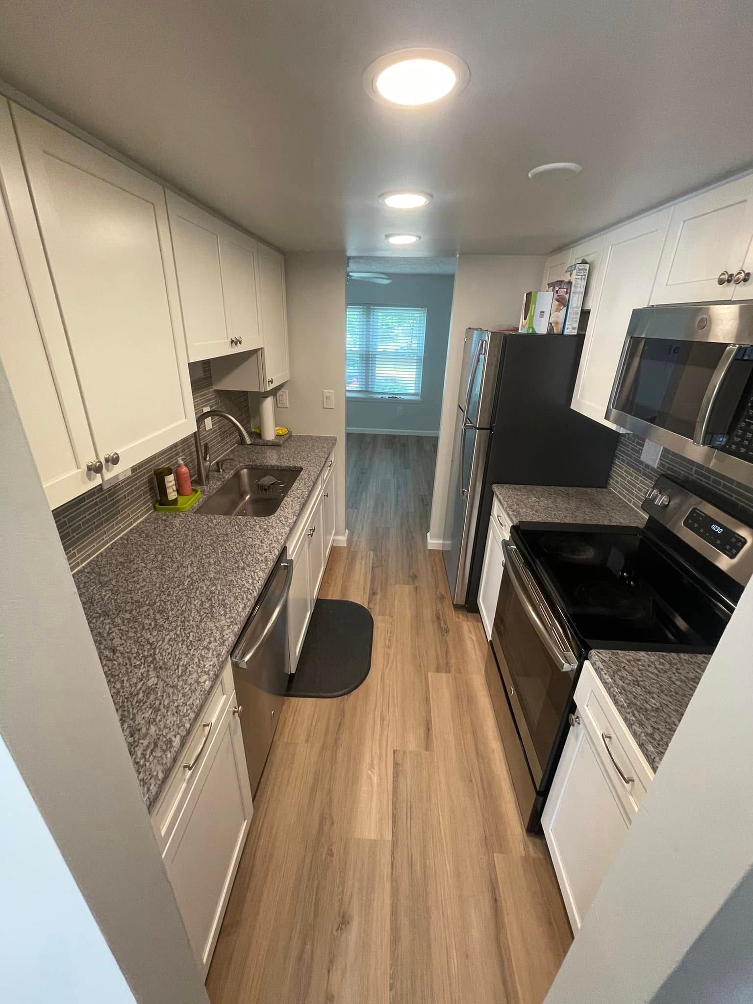 Narrow galley kitchen with white cabinets, black appliances, granite counters, and wood-look floor.