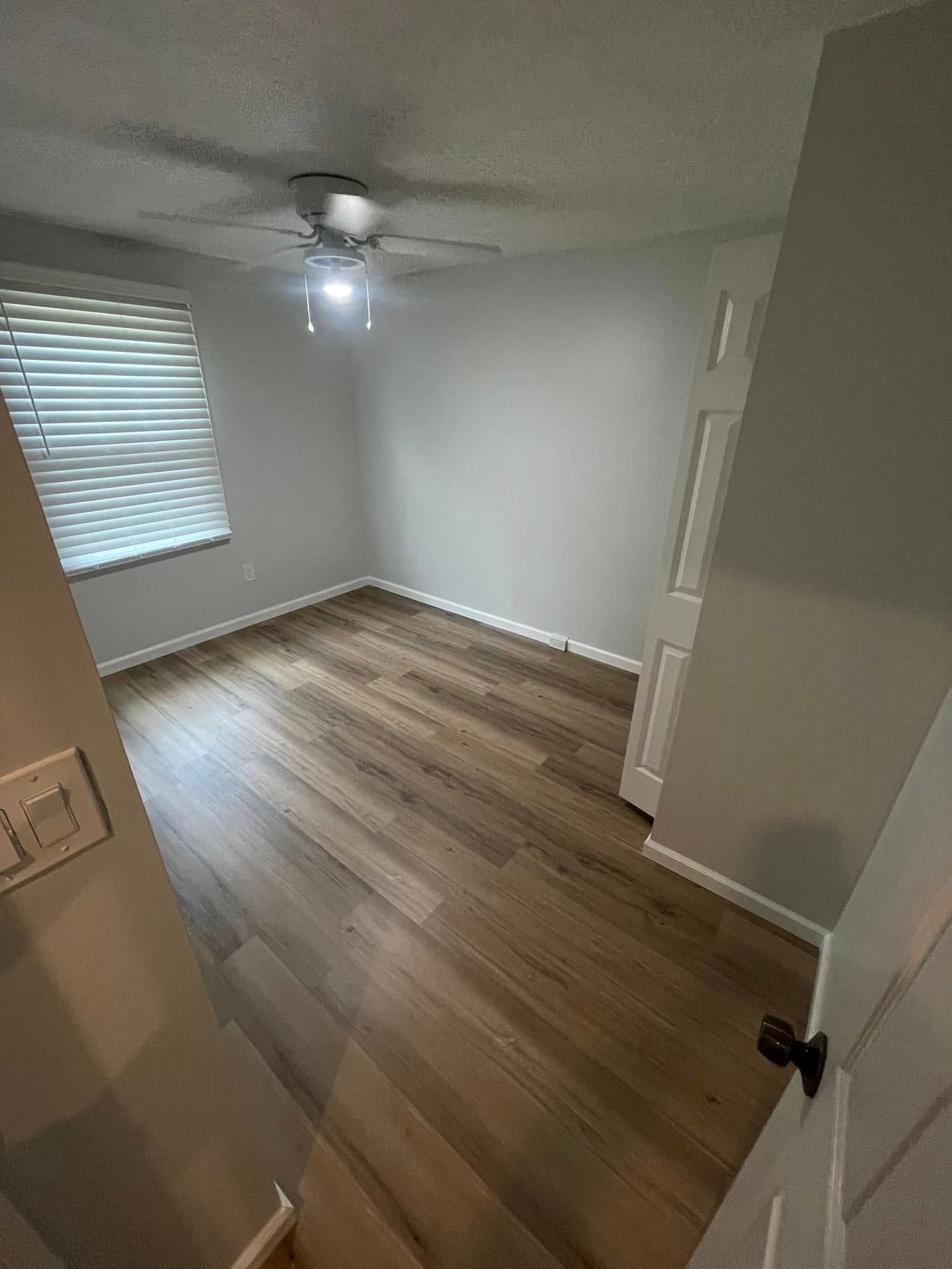 Empty unfurnished bedroom with wood flooring, white walls, a ceiling fan, and a window with blinds.
